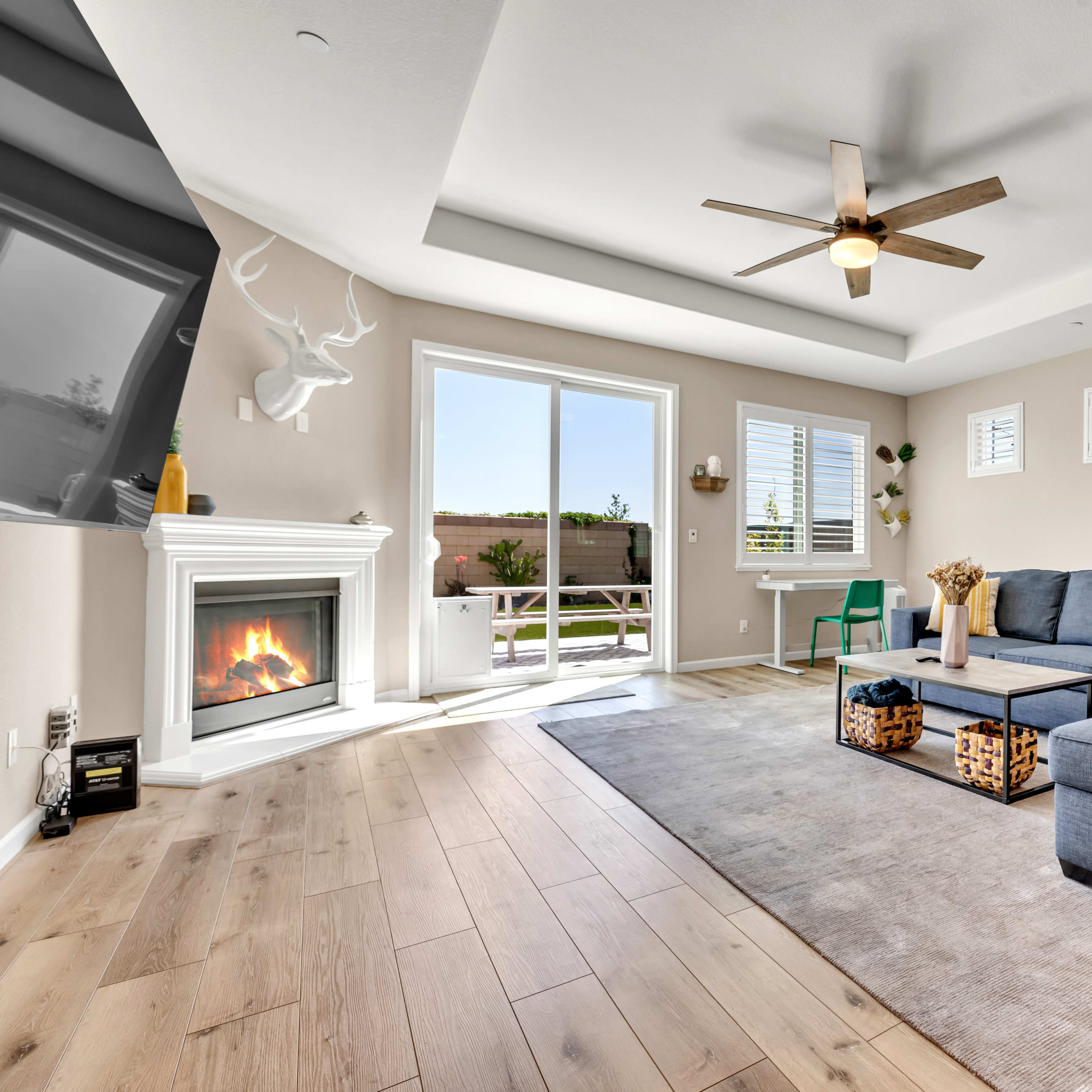 A modern living room with a gray sectional sofa, a fireplace, and large windows allowing natural light to enter.