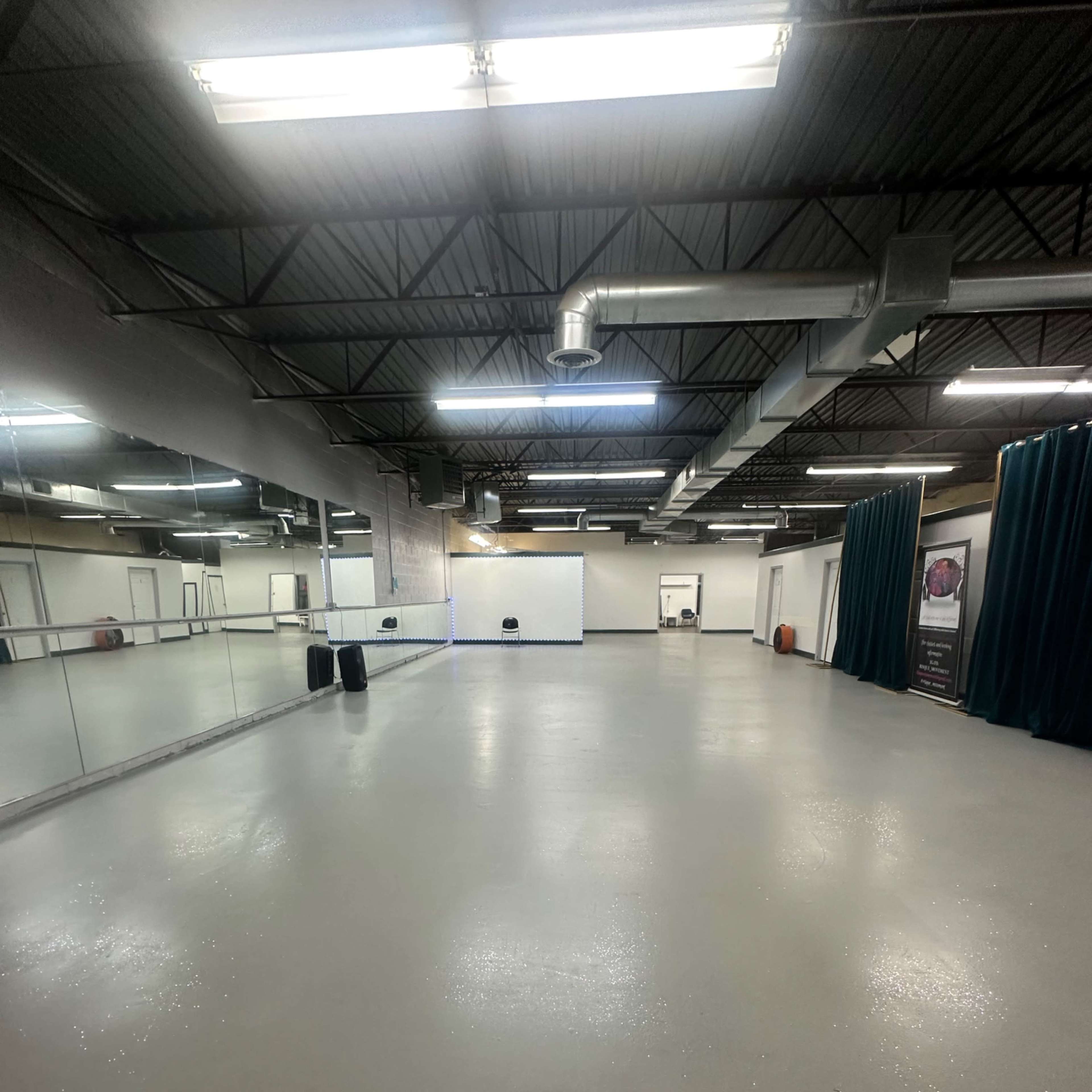 A spacious, empty room with a polished floor, large mirrors on one wall, and green curtains in the background.