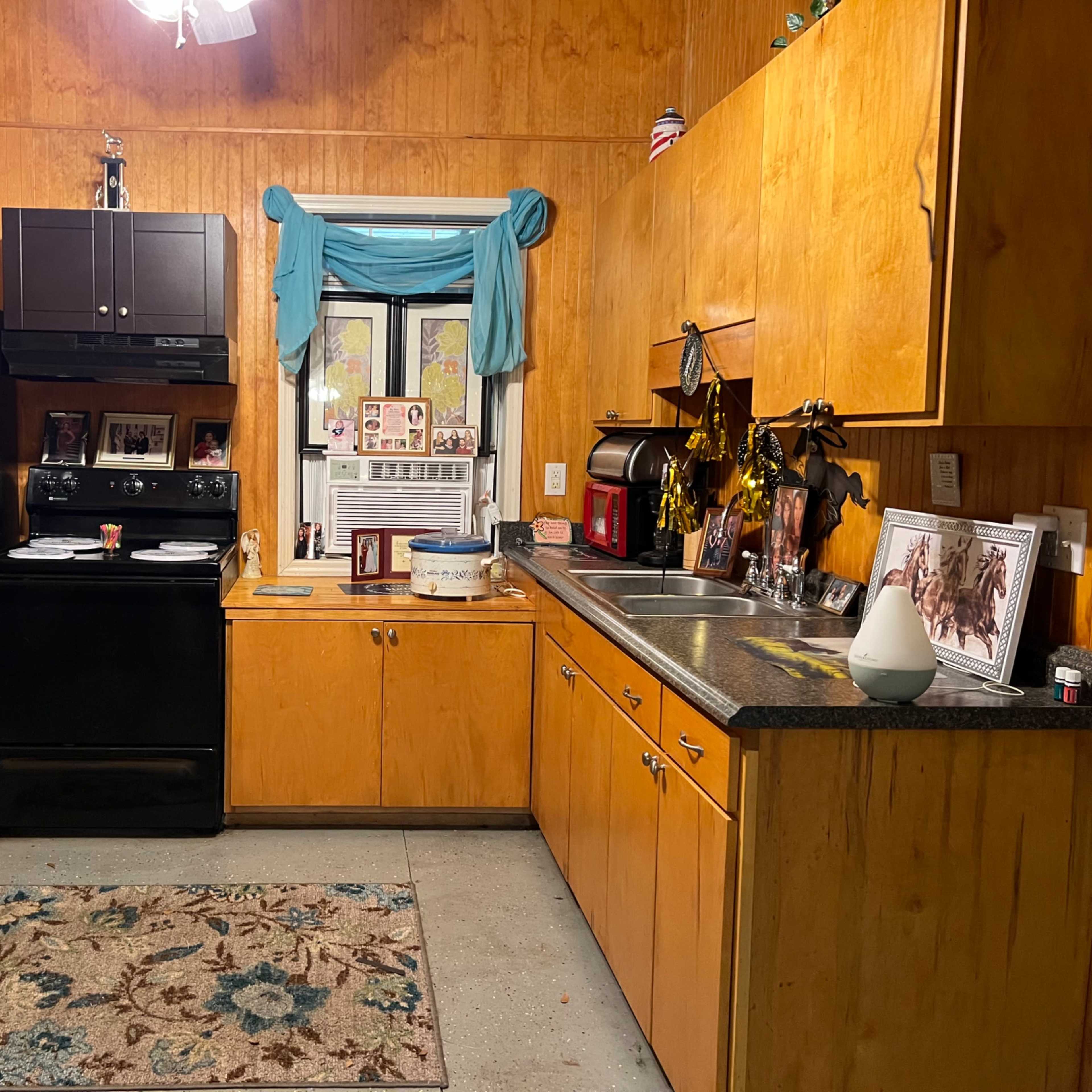 A kitchen with wooden paneling, a refrigerator, a stove, a sink, and a small rug on the floor.