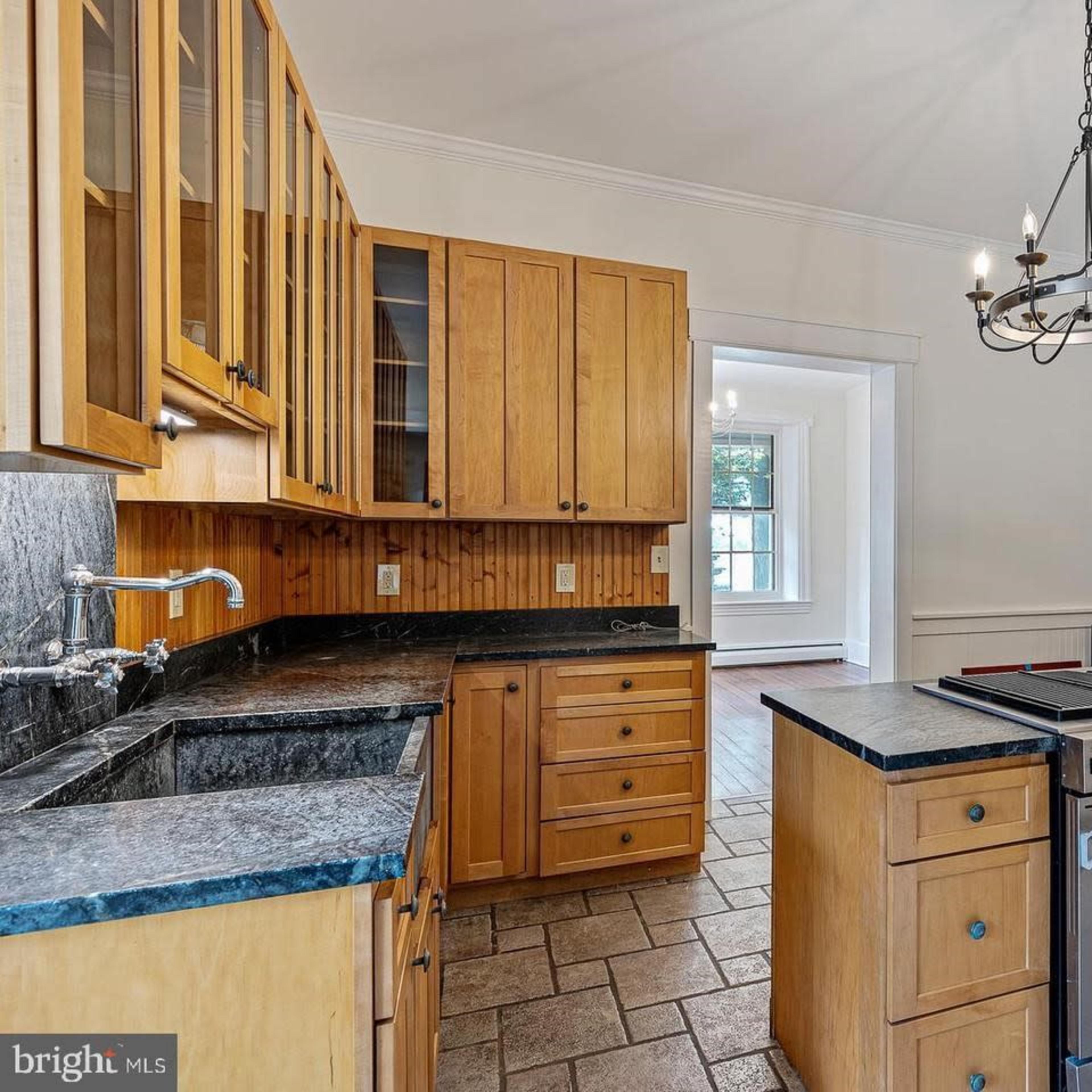 The kitchen features wooden cabinetry, a central island with a stove, and stone tile flooring.
