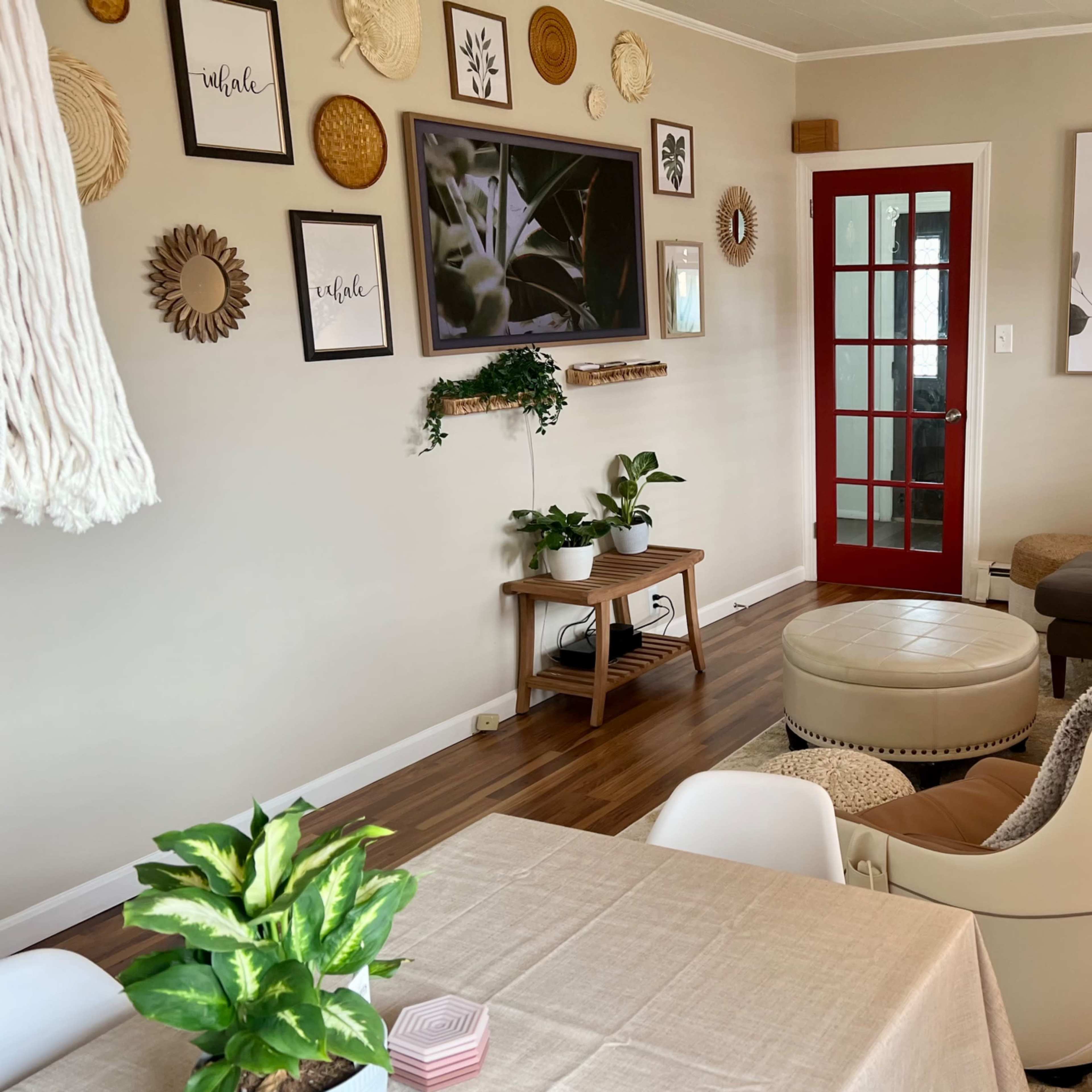A cozy living room features a mix of wall art, plants, a chaise lounge, and a red door leading to another space.