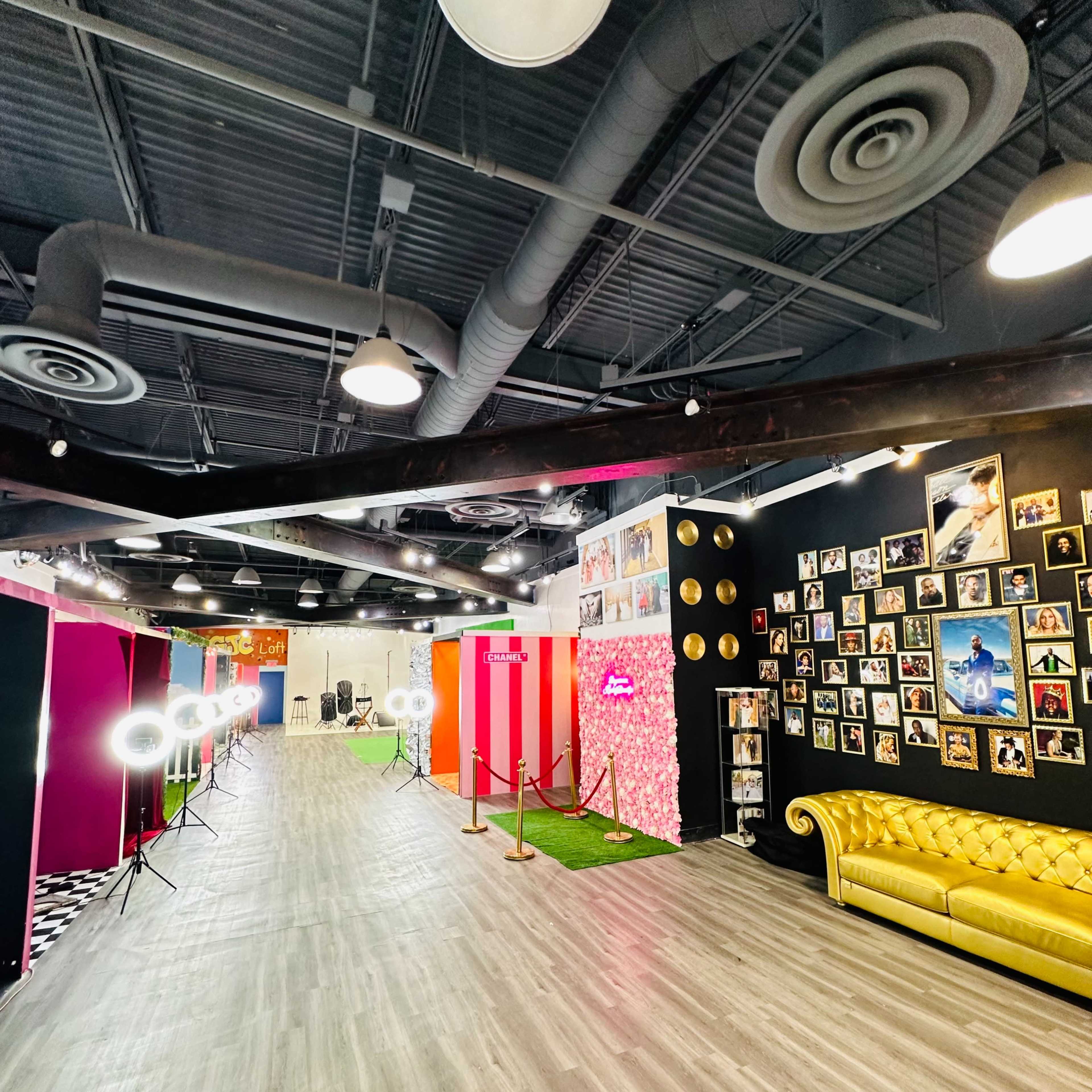 A spacious event venue featuring a yellow couch, photo booths with colorful backdrops, and a gallery wall of framed photos.