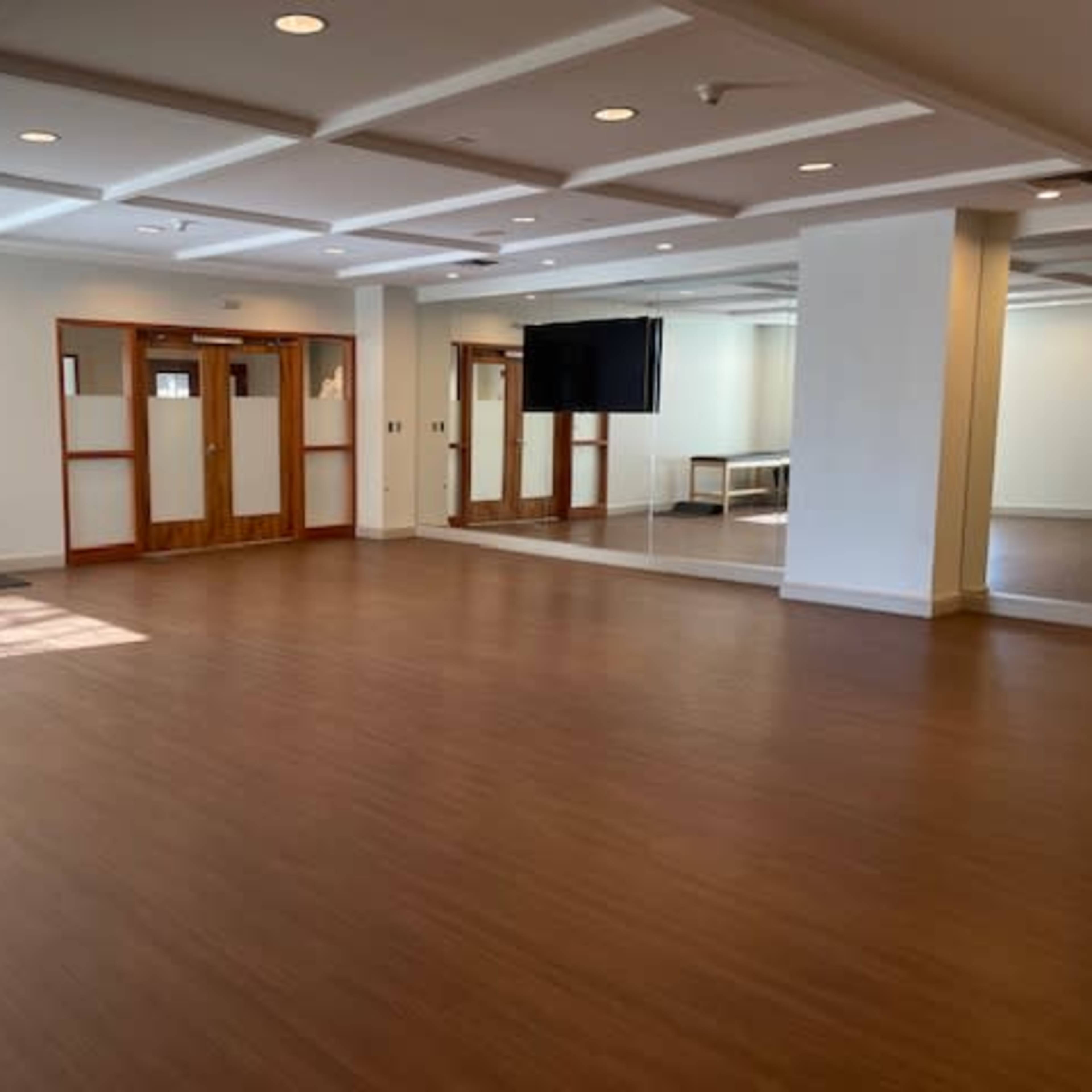 A spacious room with wooden flooring, large mirrors on one wall, and double doors leading to another area.