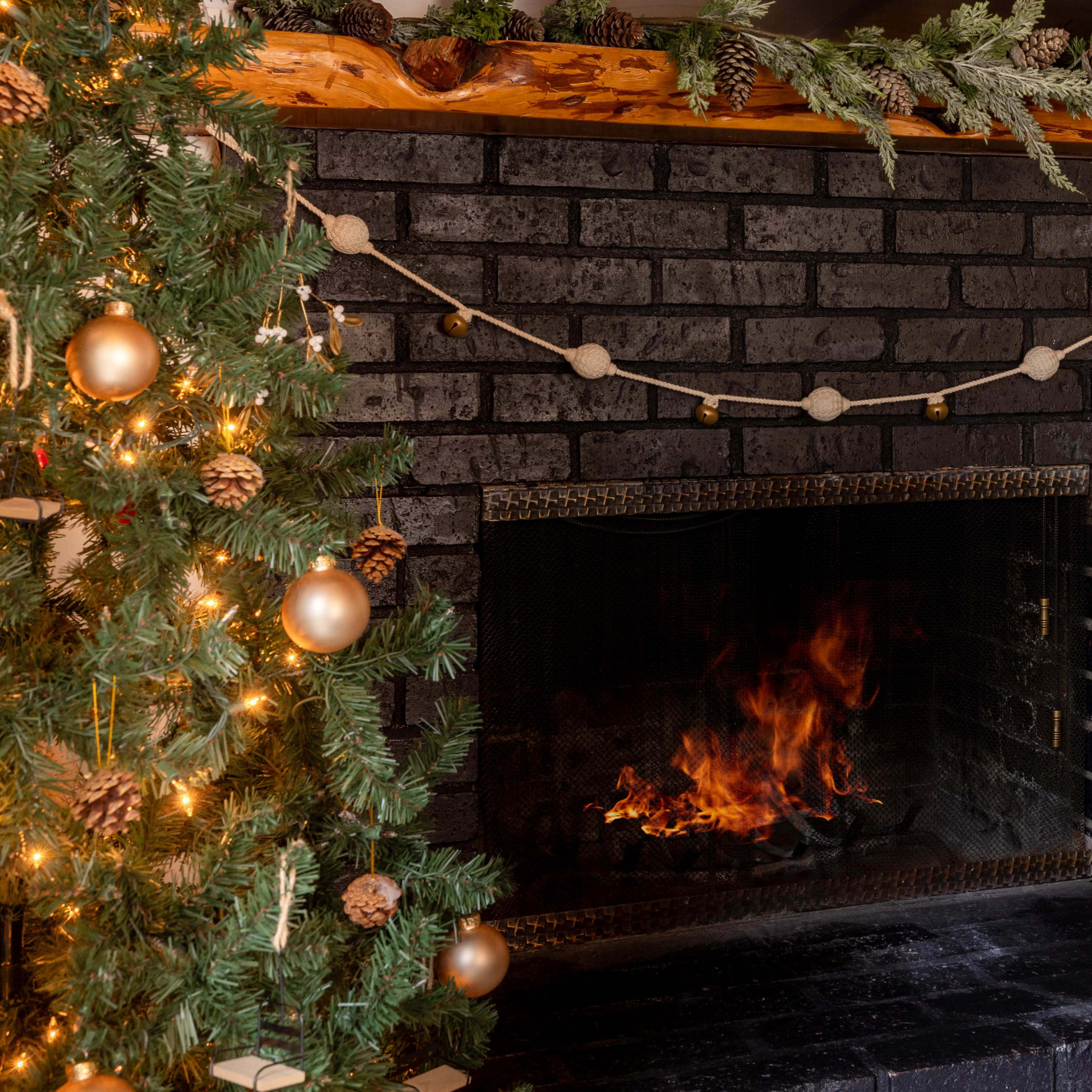 A cozy fireplace with a black brick surround features a small fire burning, while a decorated Christmas tree stands nearby.