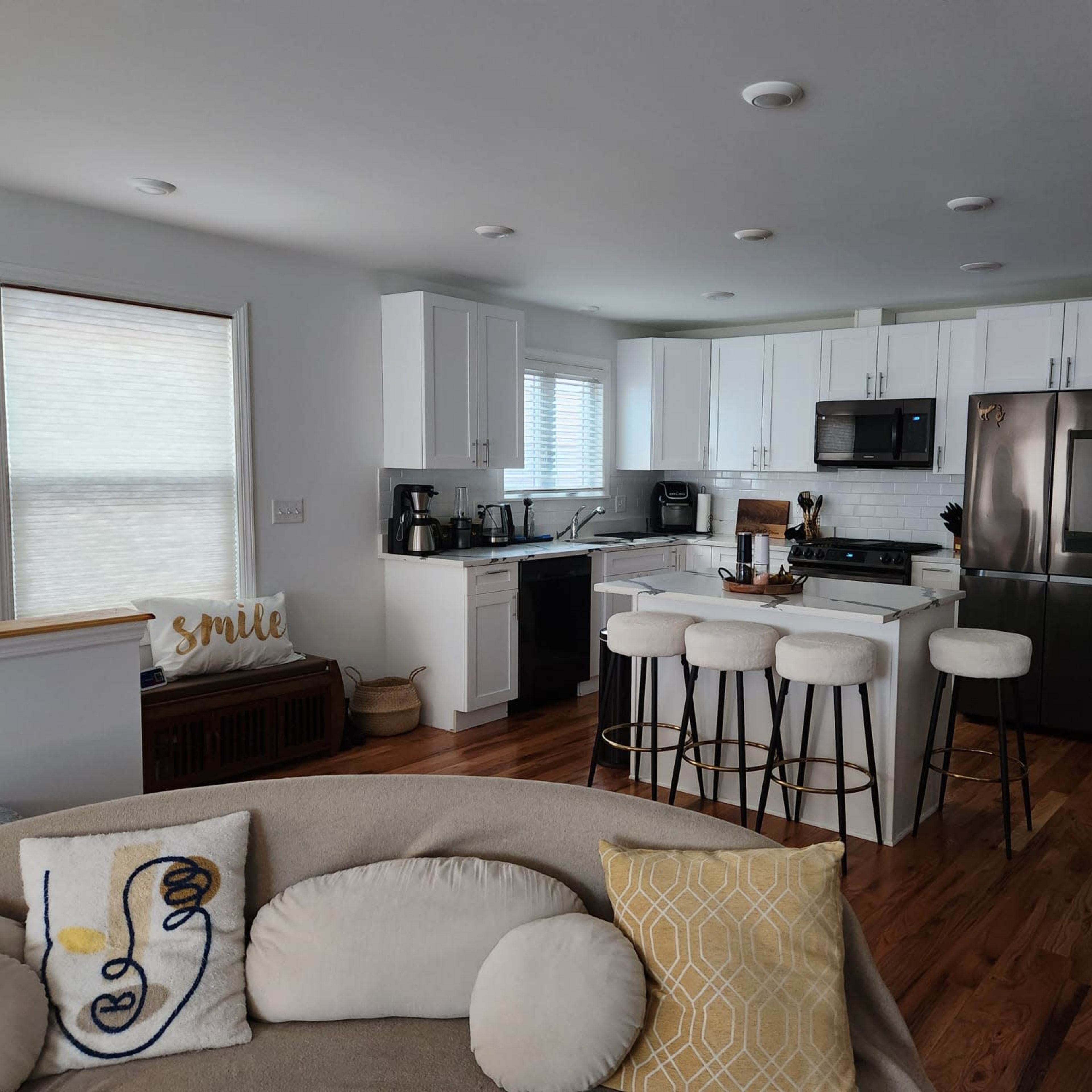 A modern kitchen with white cabinetry, stainless steel appliances, and a dining area featuring bar stools and a round table.