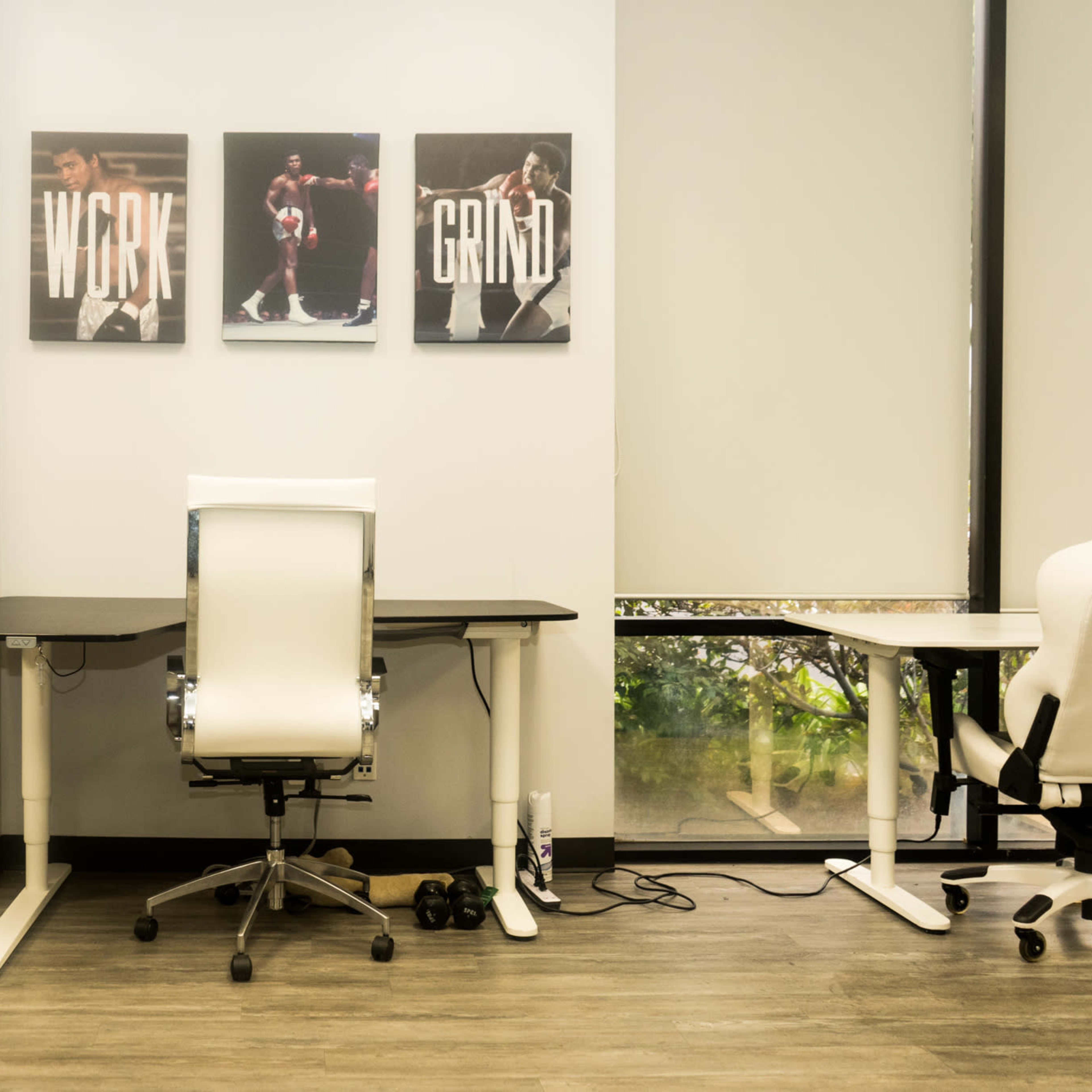 A minimalist office space featuring two desks, a black chair, and three framed motivational posters on the wall.