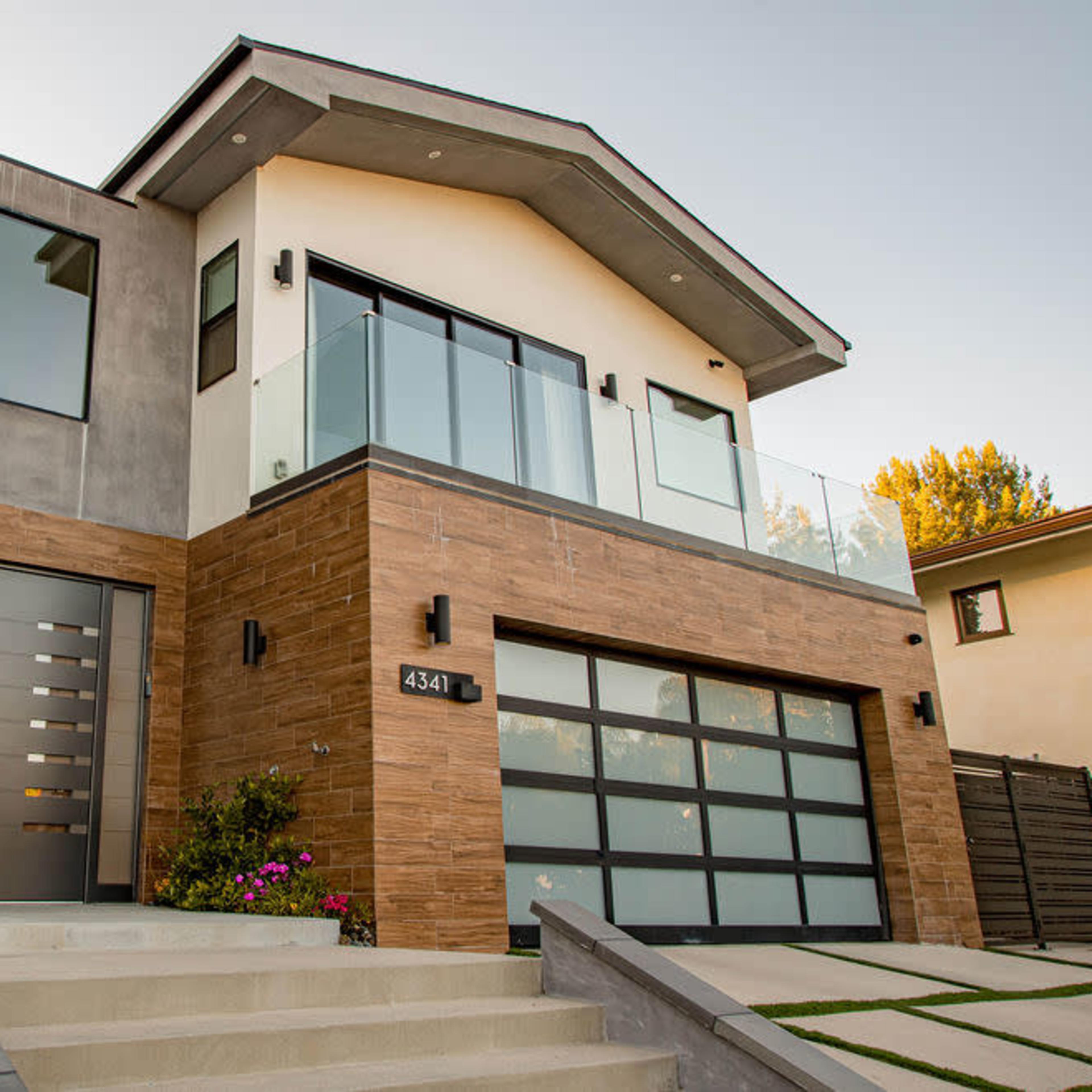 A modern two-story house with a combination of concrete and wood finishes, featuring large windows and a spacious front entrance with landscaped steps.