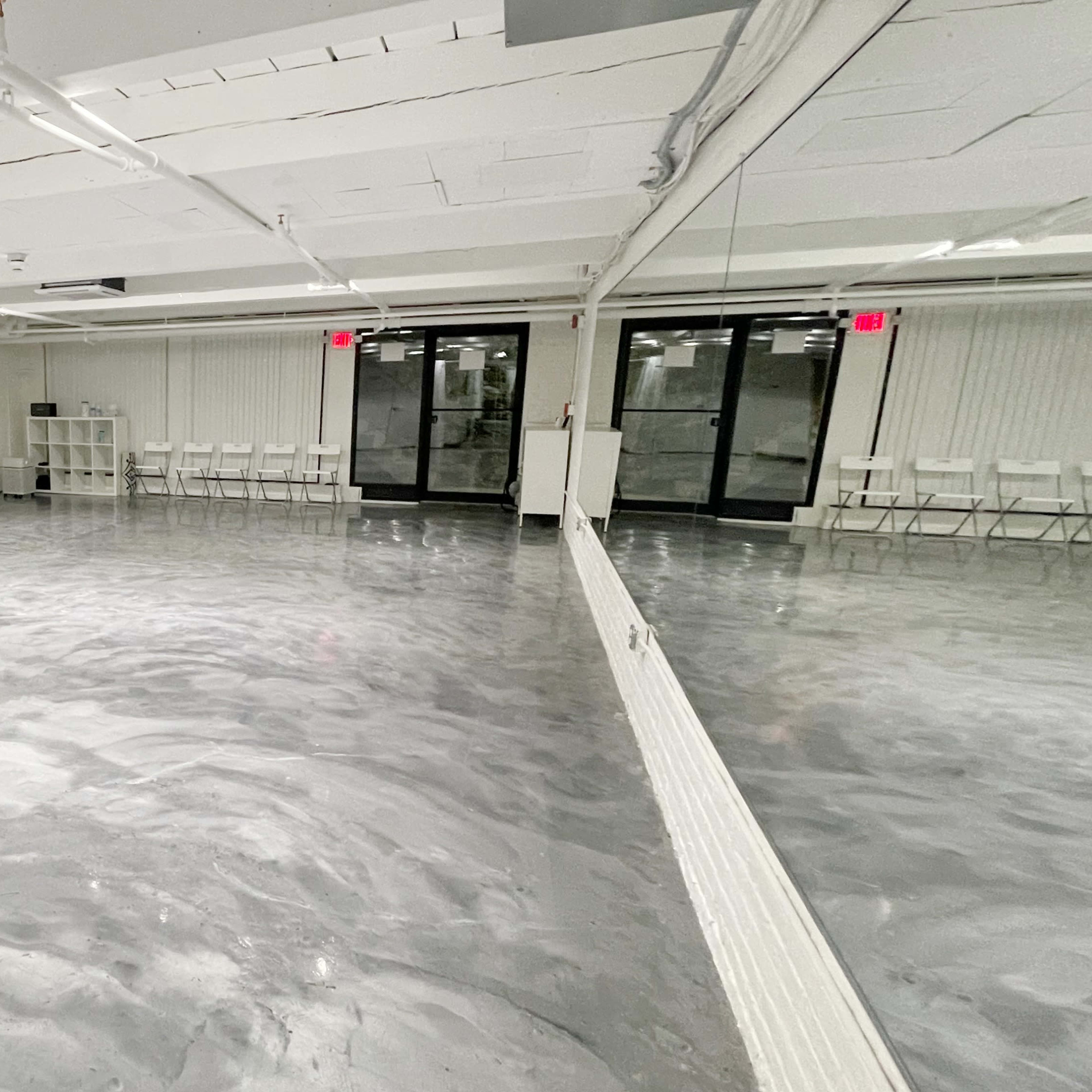 A spacious, empty studio with a polished gray concrete floor and large windows allowing natural light.