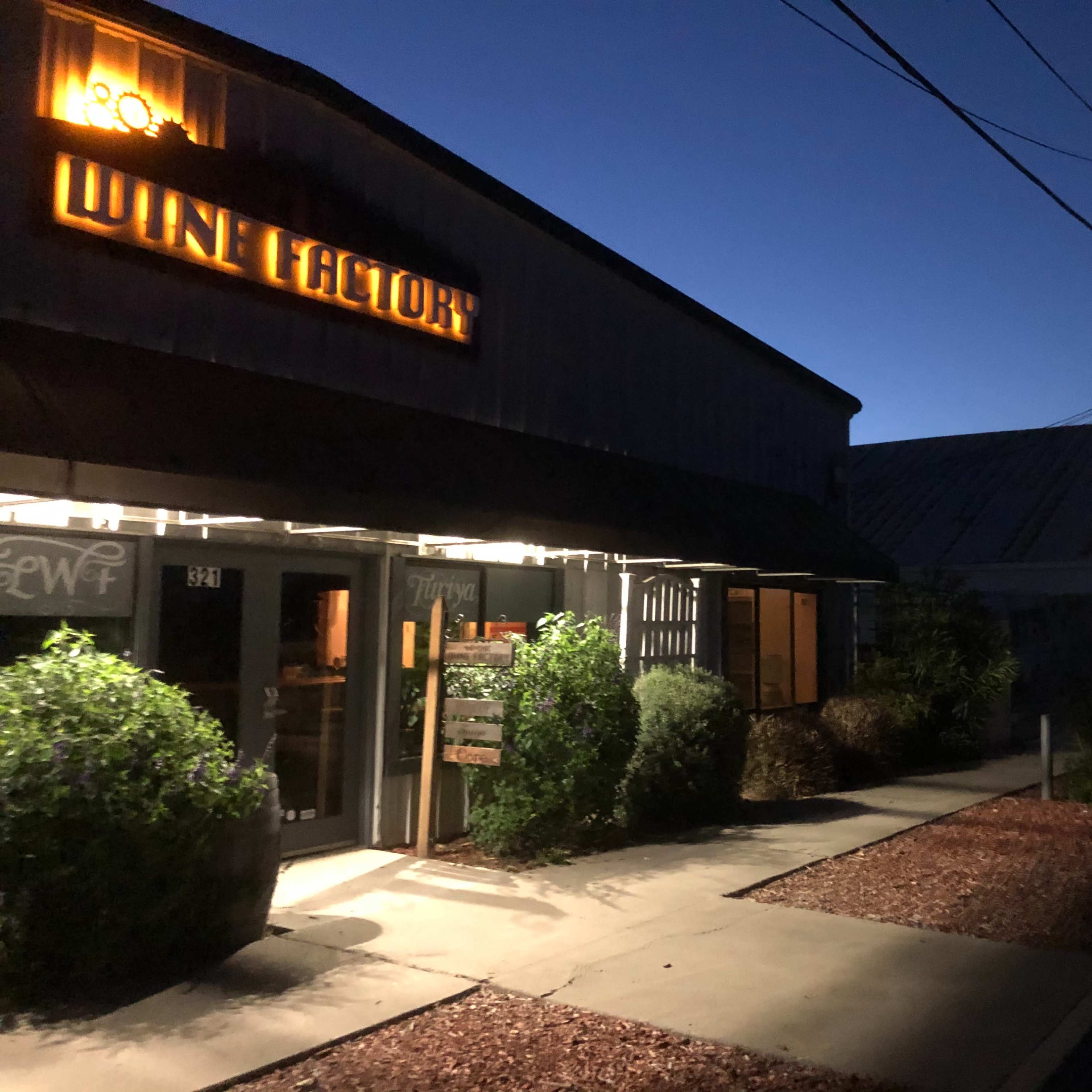 A wine store with a lit sign, set against a twilight sky, along a street lined with power lines.