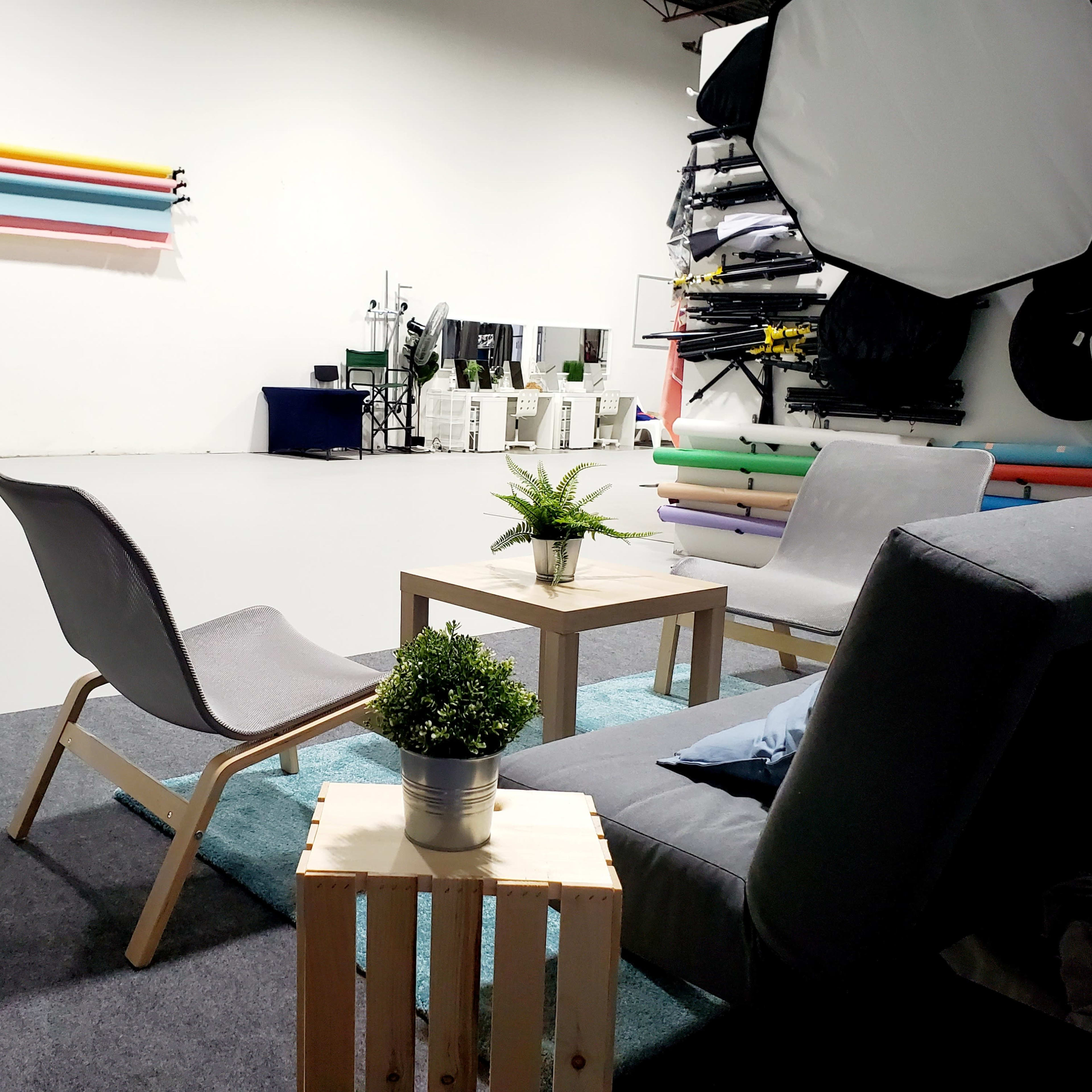 A photography studio with grey furniture, a small table, and colorful backdrops mounted on the wall.
