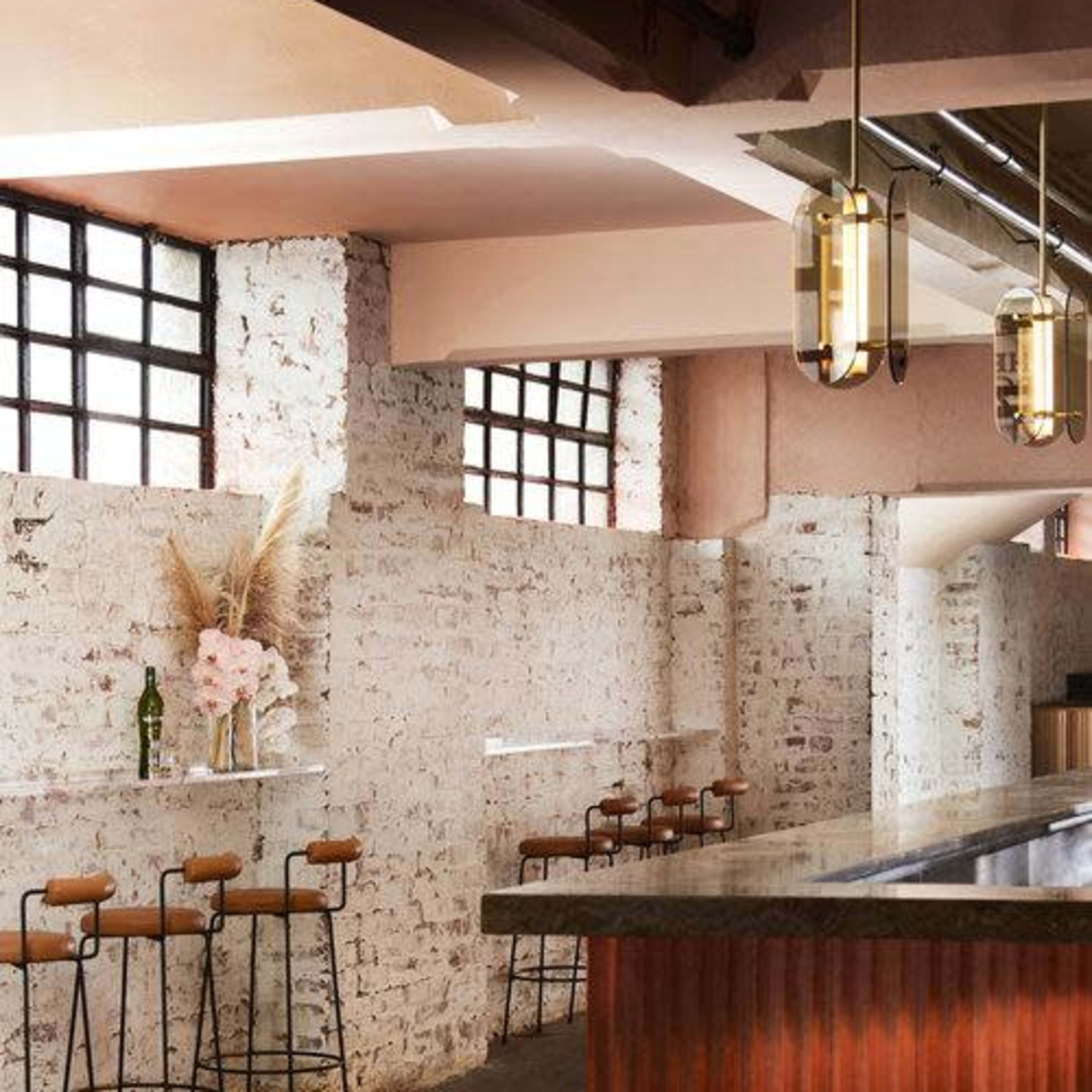 A modern bar area with high stools along a brick wall and a polished countertop, illuminated by contemporary pendant lights.