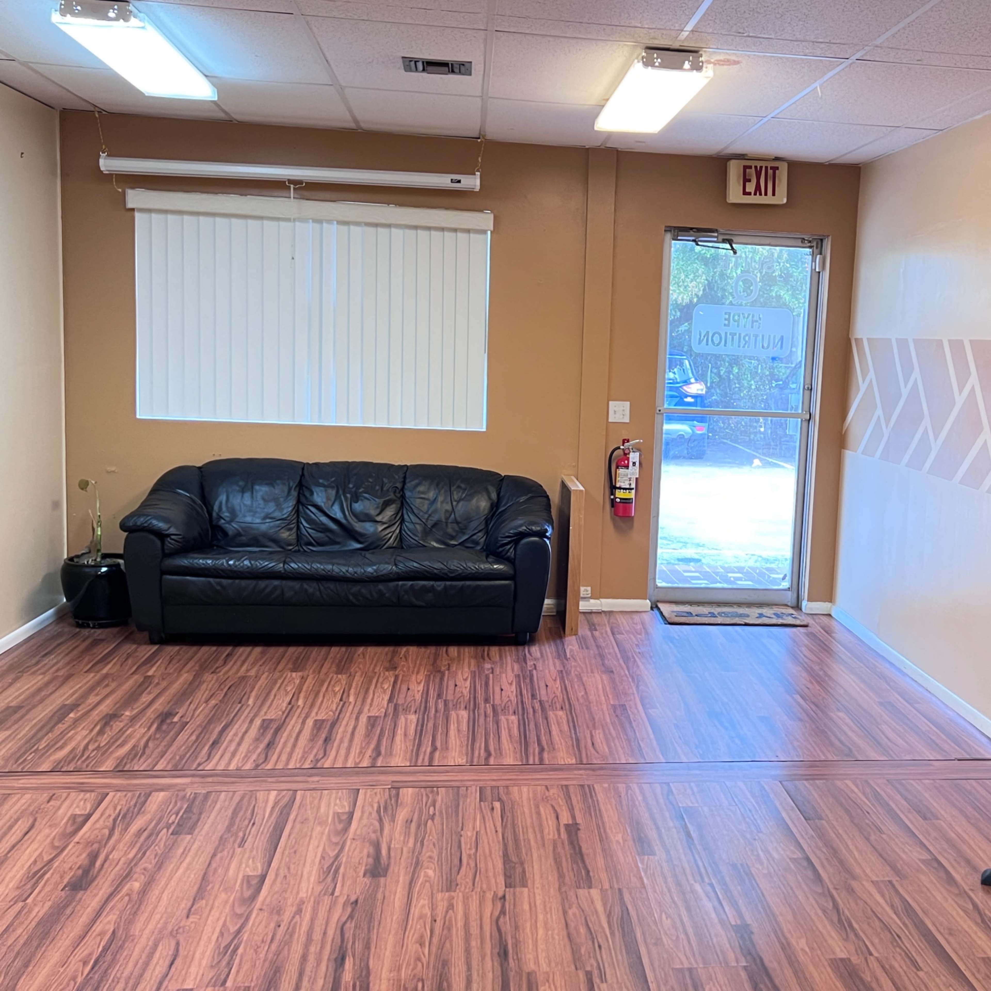 A room with a black leather couch, a small round table, and a door leading outside.
