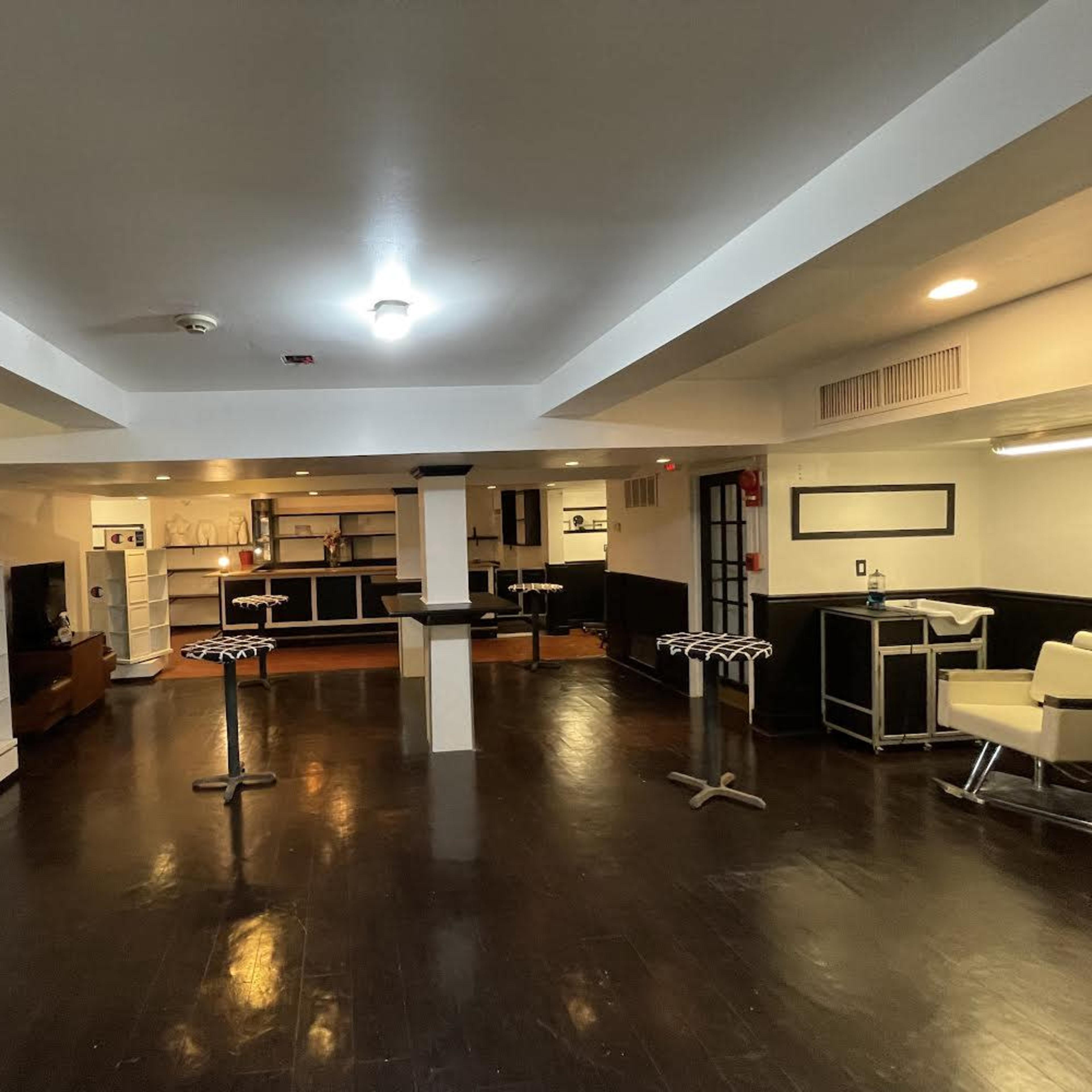 A spacious, well-lit interior features a mixture of seating areas, a bar counter, and shelves, with dark flooring and white walls.