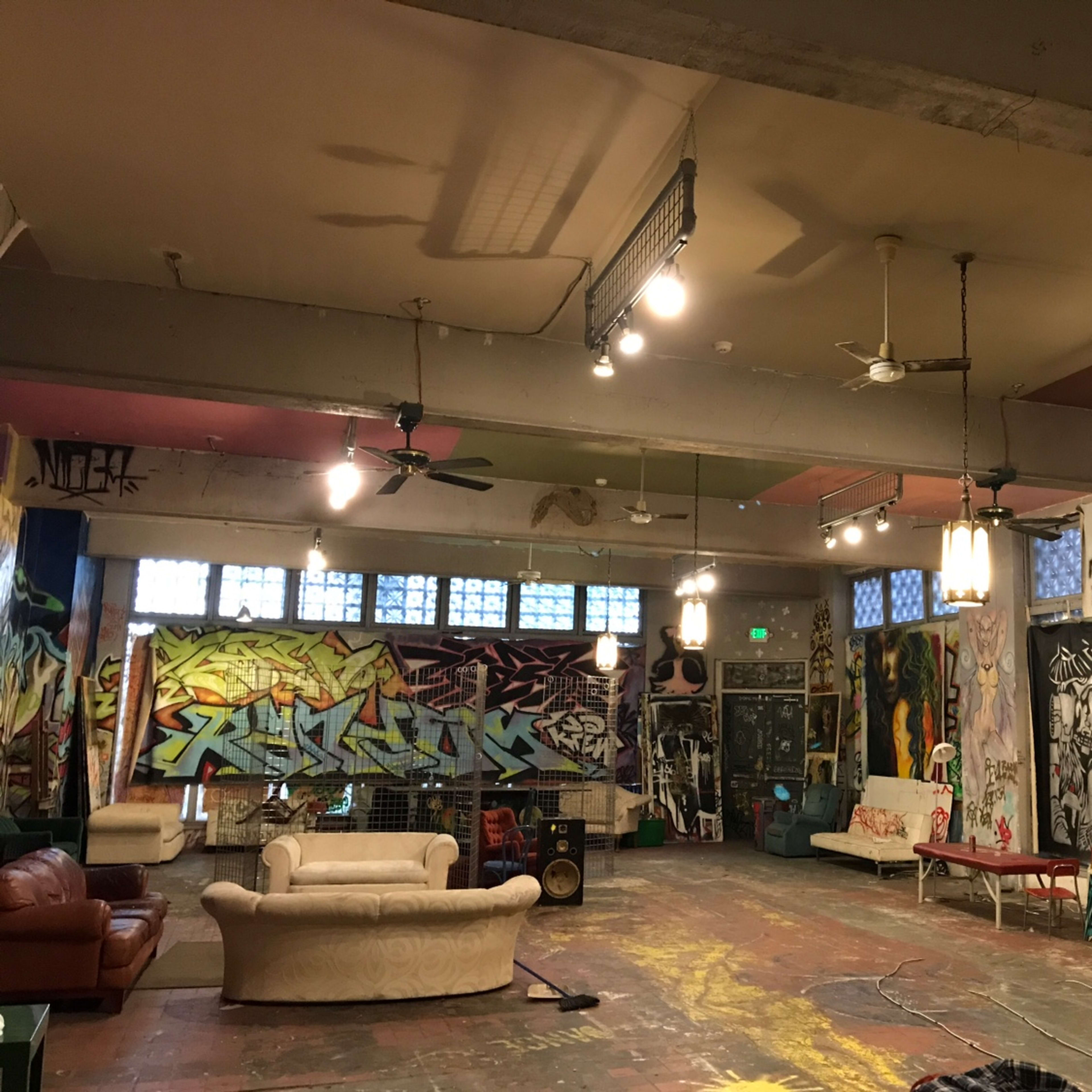 A large, open room with colorful graffiti-covered walls, multiple light fixtures, and various furniture pieces scattered around.