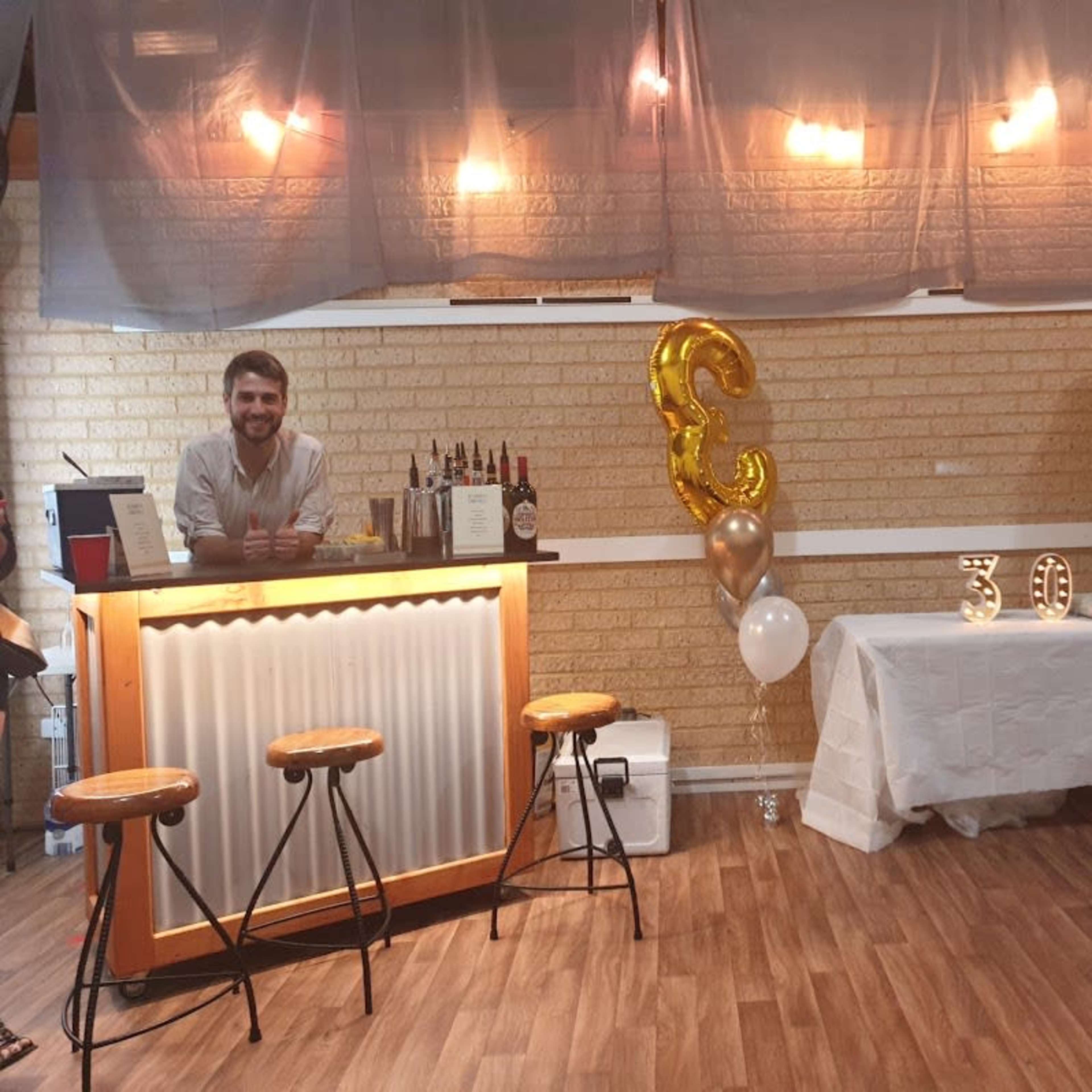 A bar setup is featured with a bartender behind the counter, a table decorated with balloons, and a sign displaying the number "30."