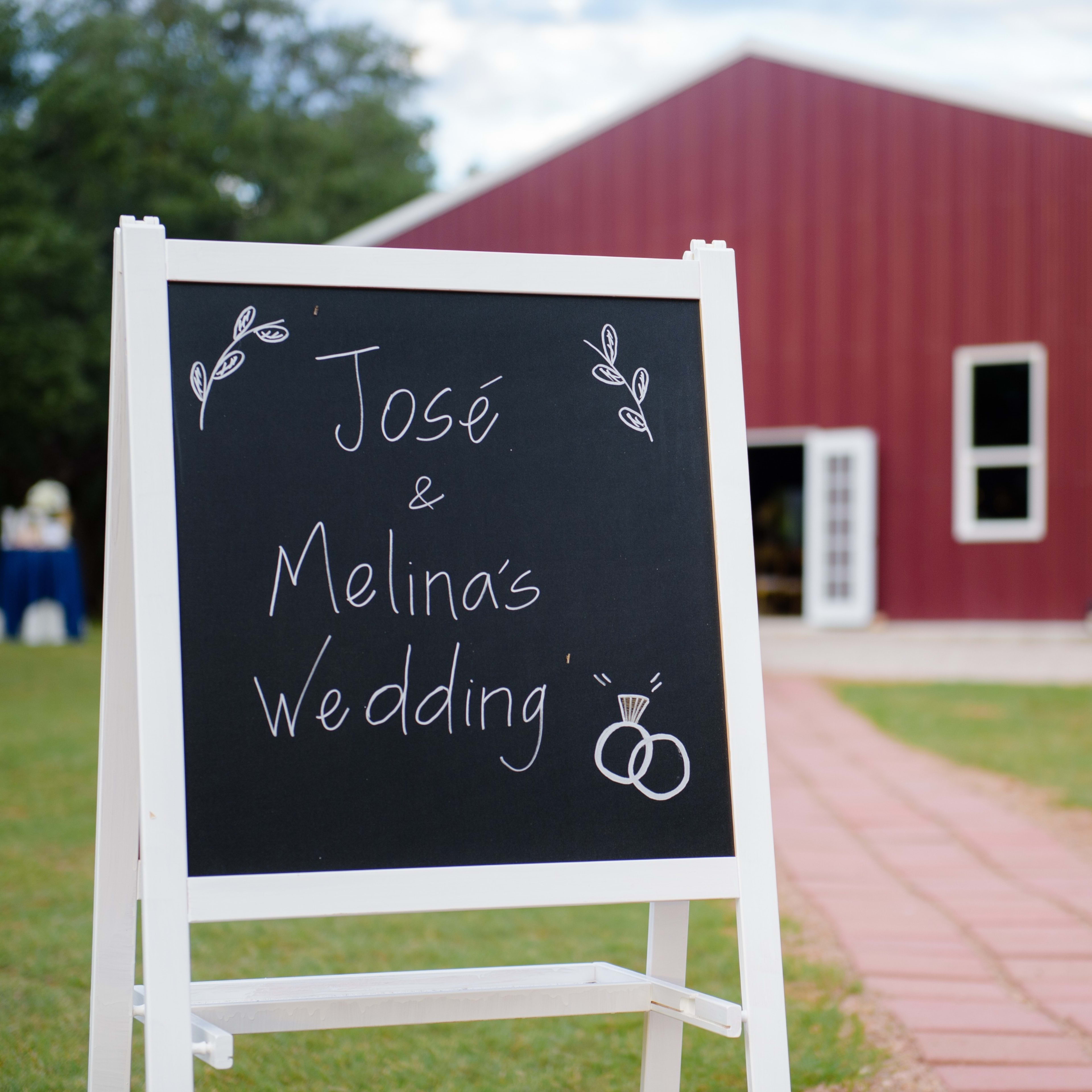 A chalkboard sign announces "José & Melina's Wedding" in front of a red barn-style venue.