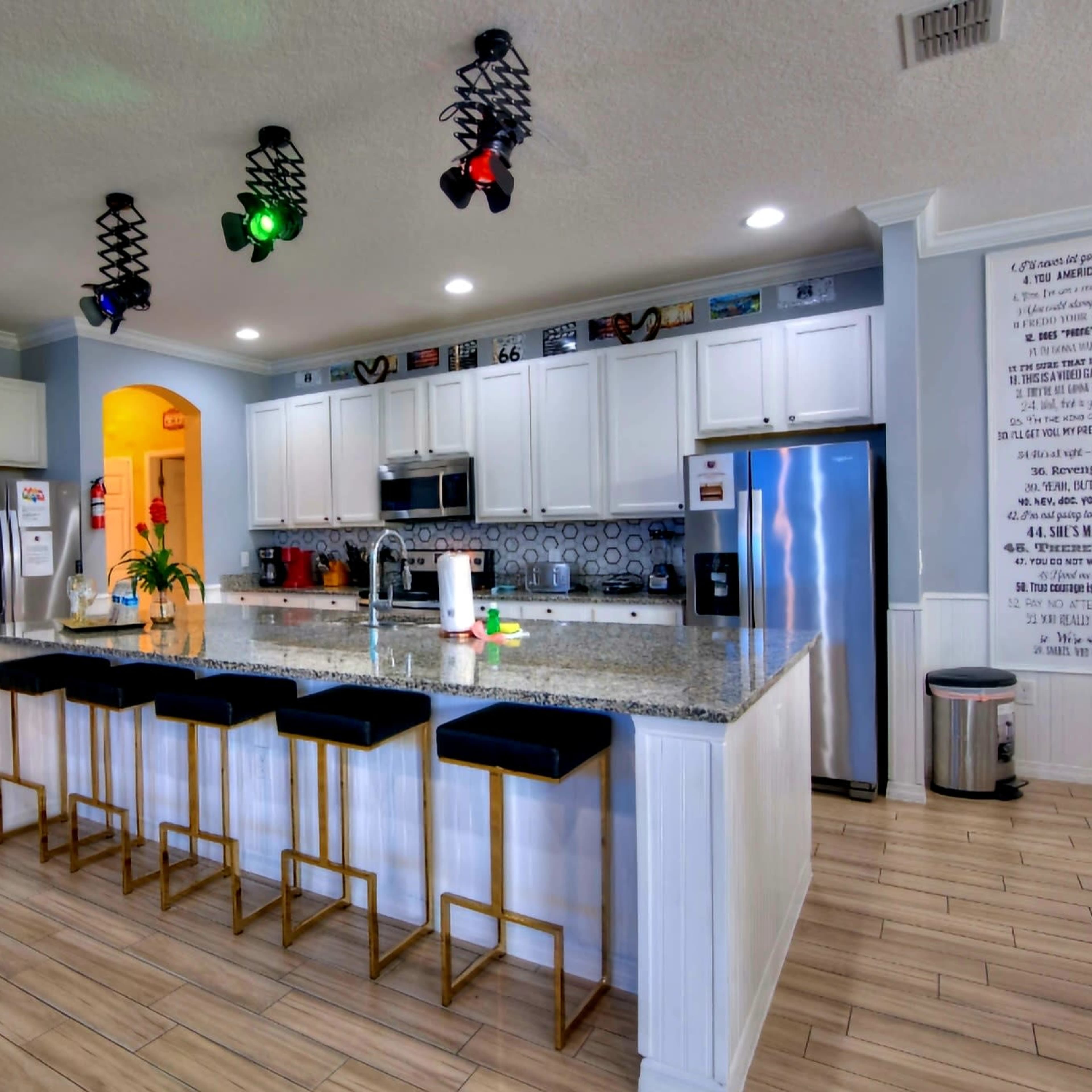 A modern kitchen with a central island, featuring white cabinetry, granite countertops, and several bar stools.