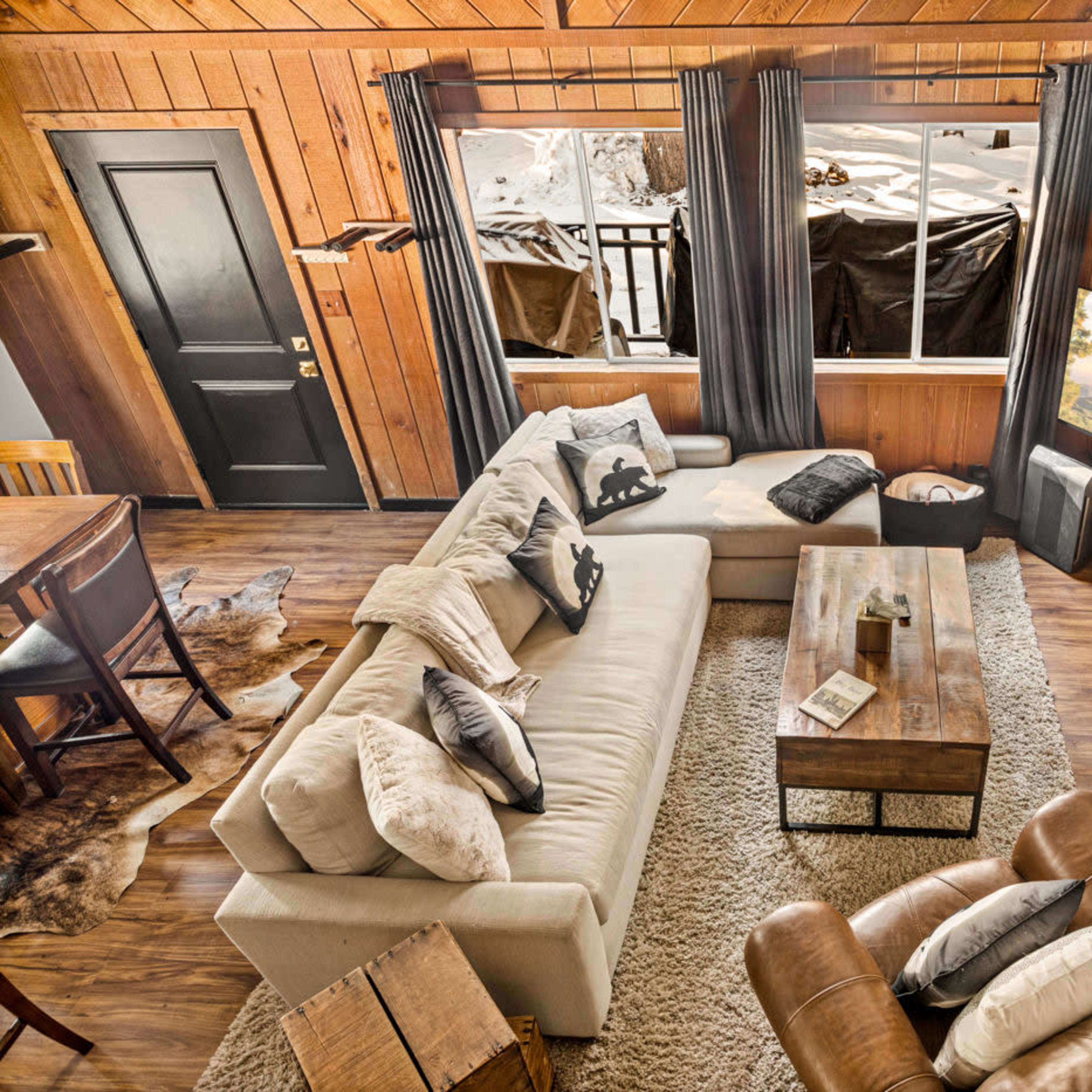 A cozy living room with a large sectional sofa, a wooden coffee table, and a brick fireplace, all illuminated by natural light from a window.