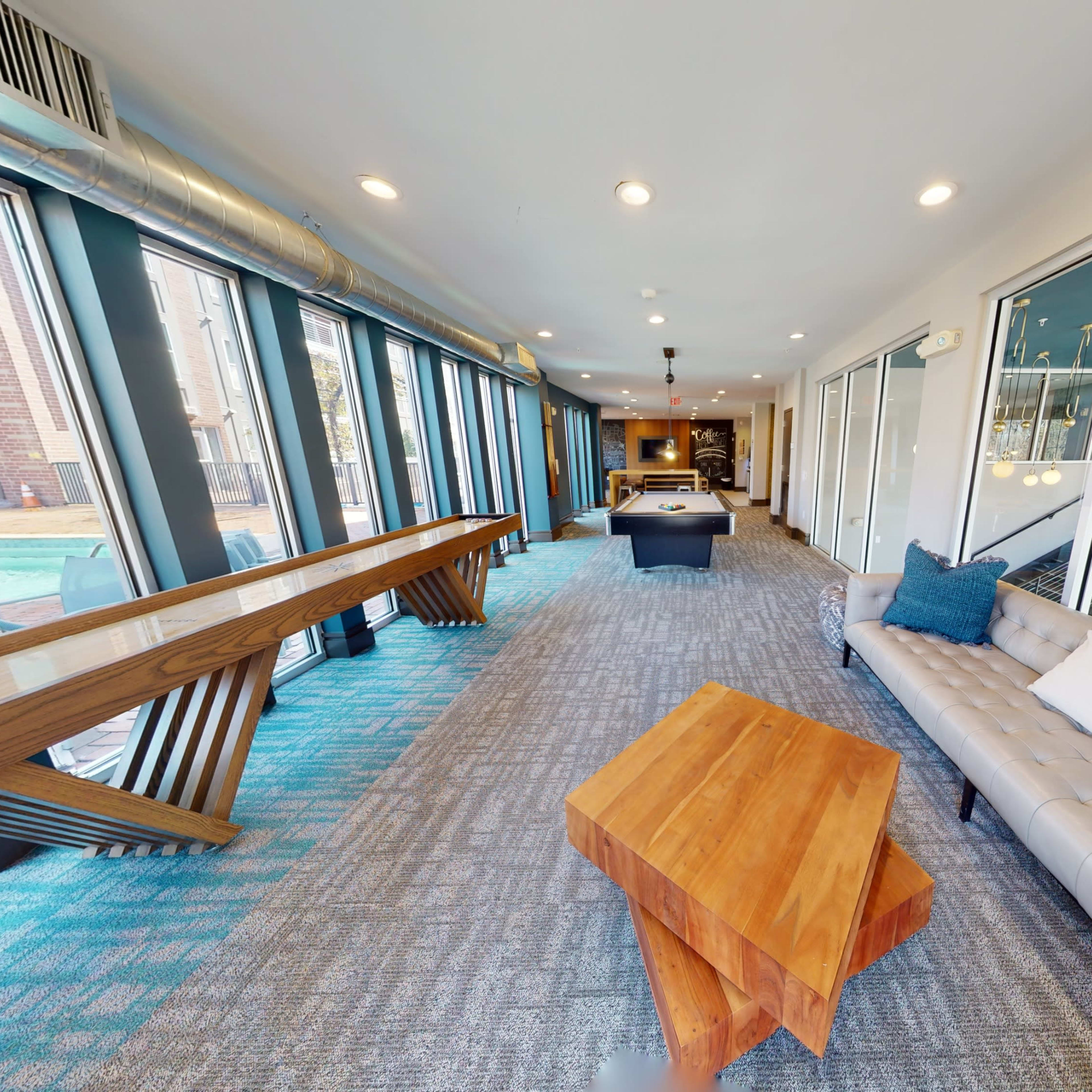 A modern lounge area with a stylish sofa, a wooden coffee table, and large windows overlooking an outdoor space.