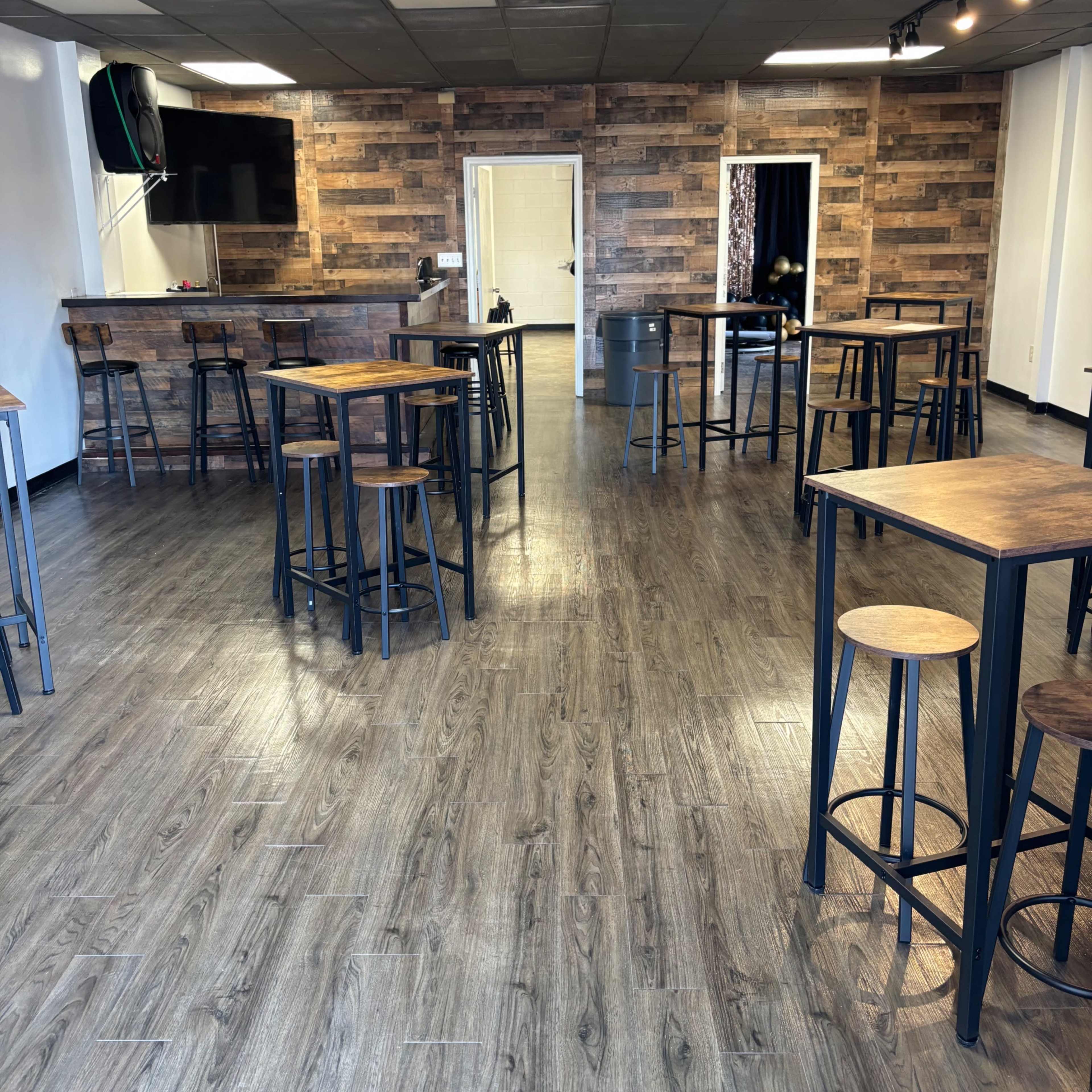 A spacious interior of a café or event space with wooden walls and multiple high tables surrounded by stools.
