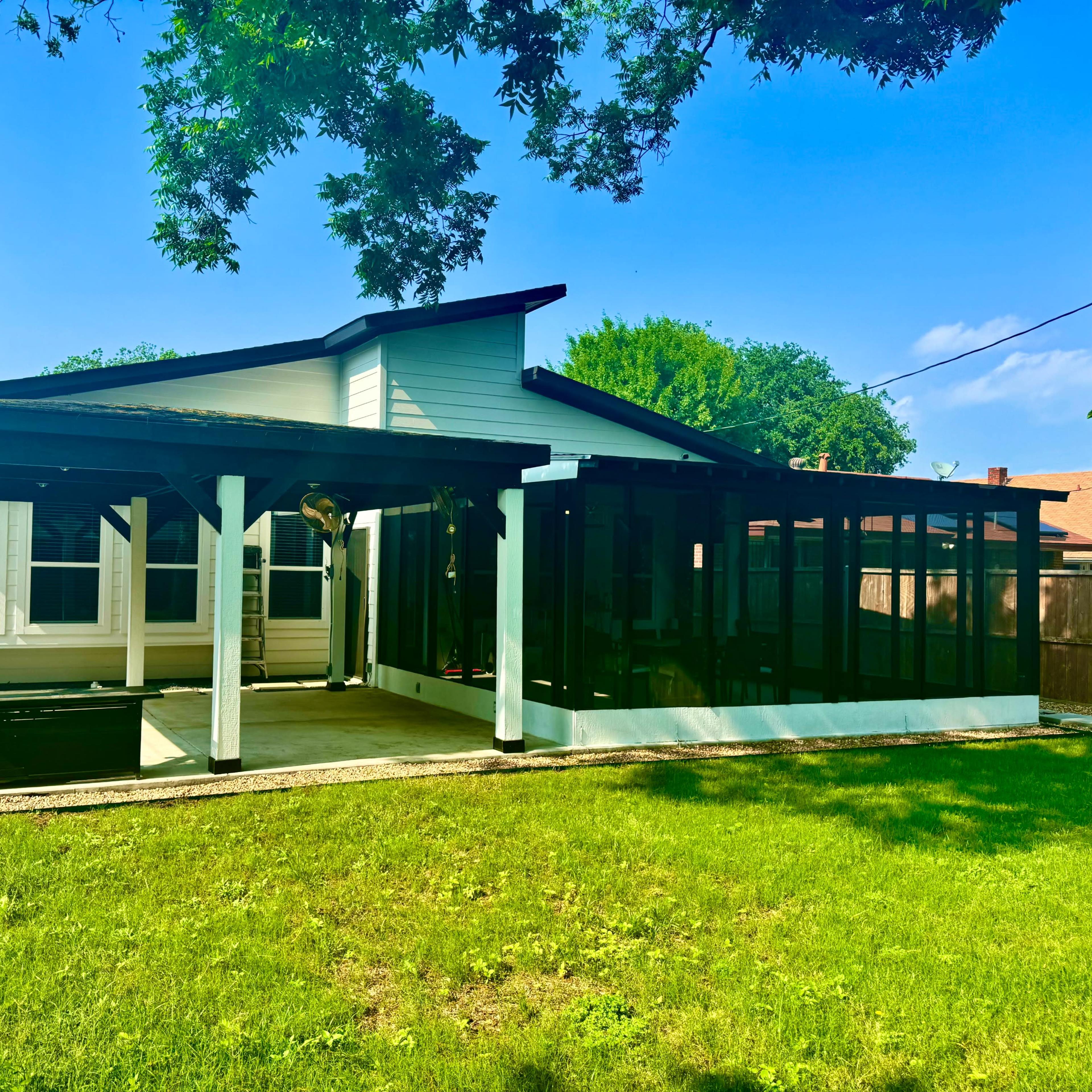 A single-story house with a large screened porch, surrounded by a lawn and trees.