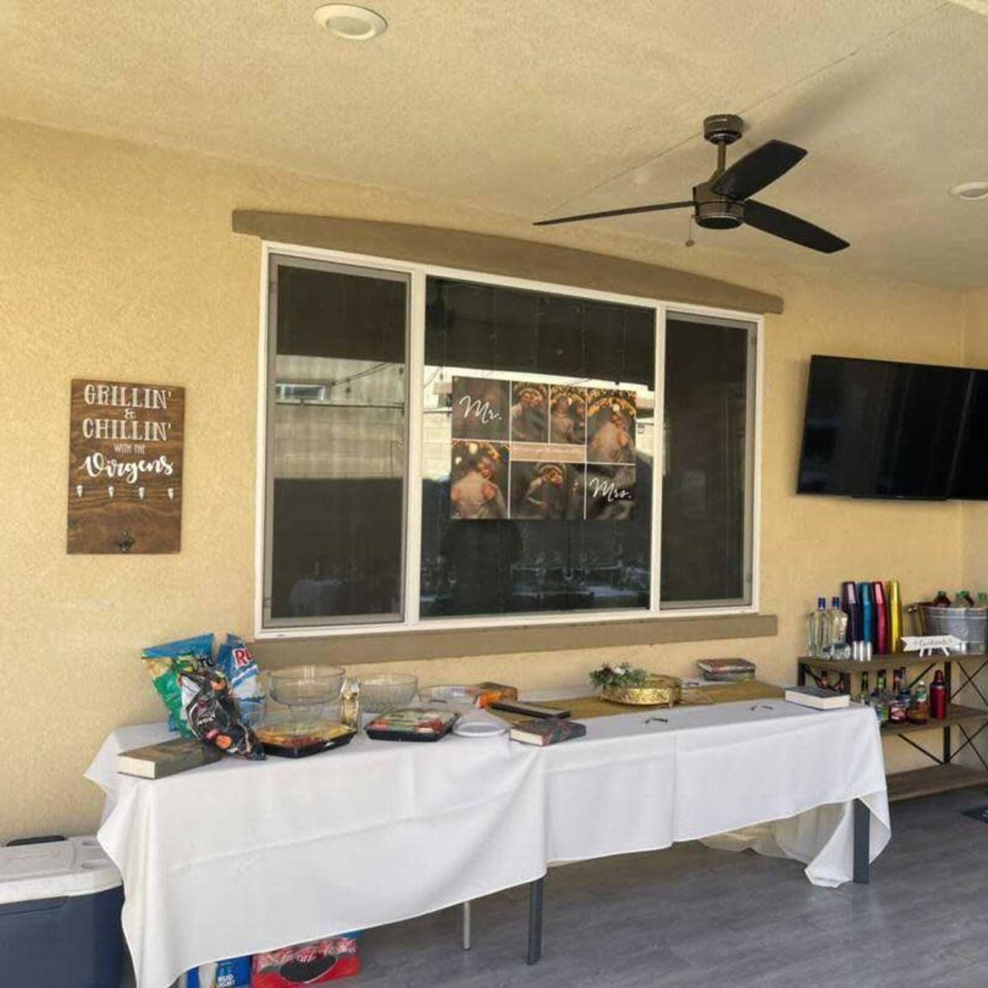 A patio area with a table covered in food, a television mounted on the wall, and a decorative sign titled "Chillin' & Grillin'" alongside framed photos.