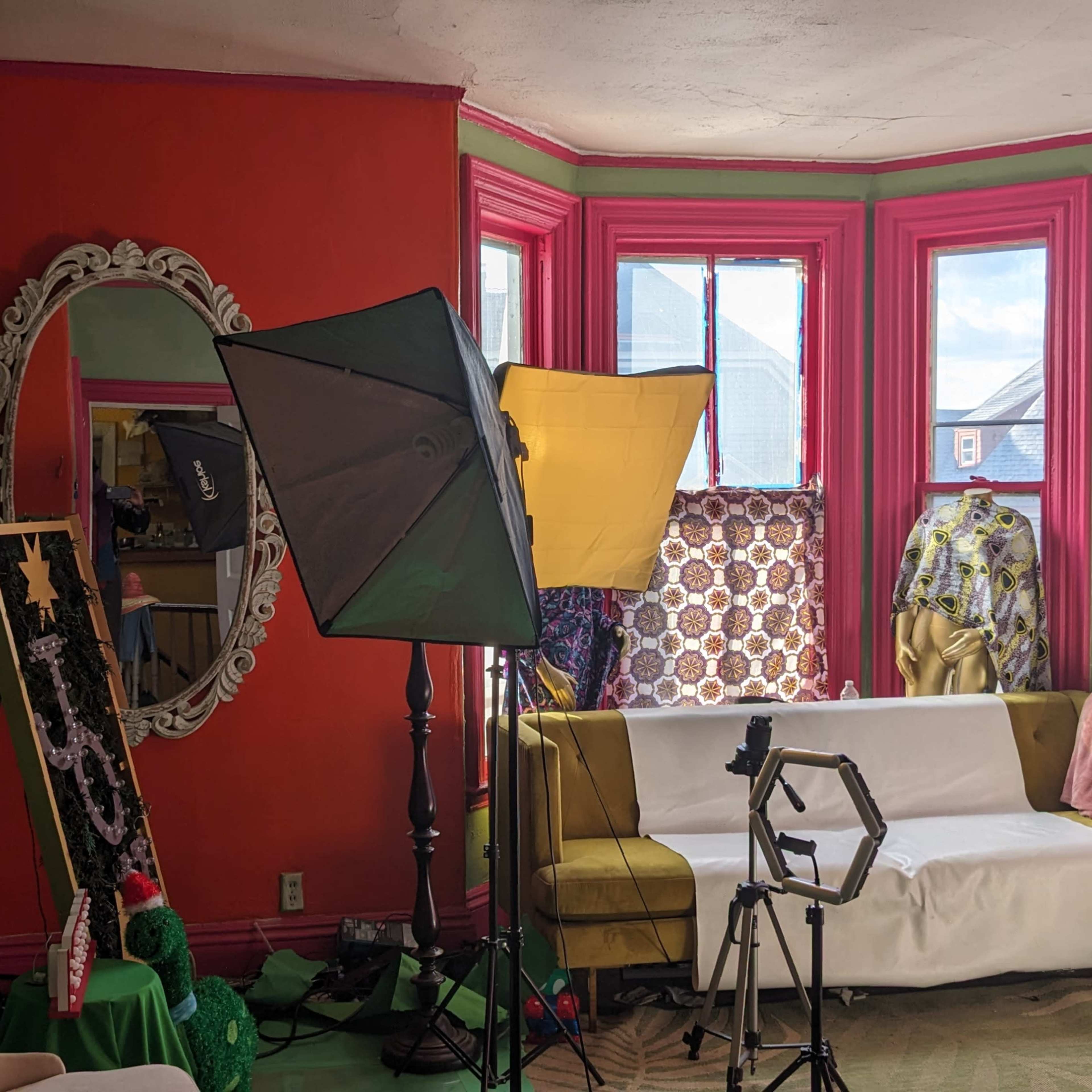 A brightly painted room with a large mirror, a sofa covered in white fabric, and various photography equipment set up for a shoot.