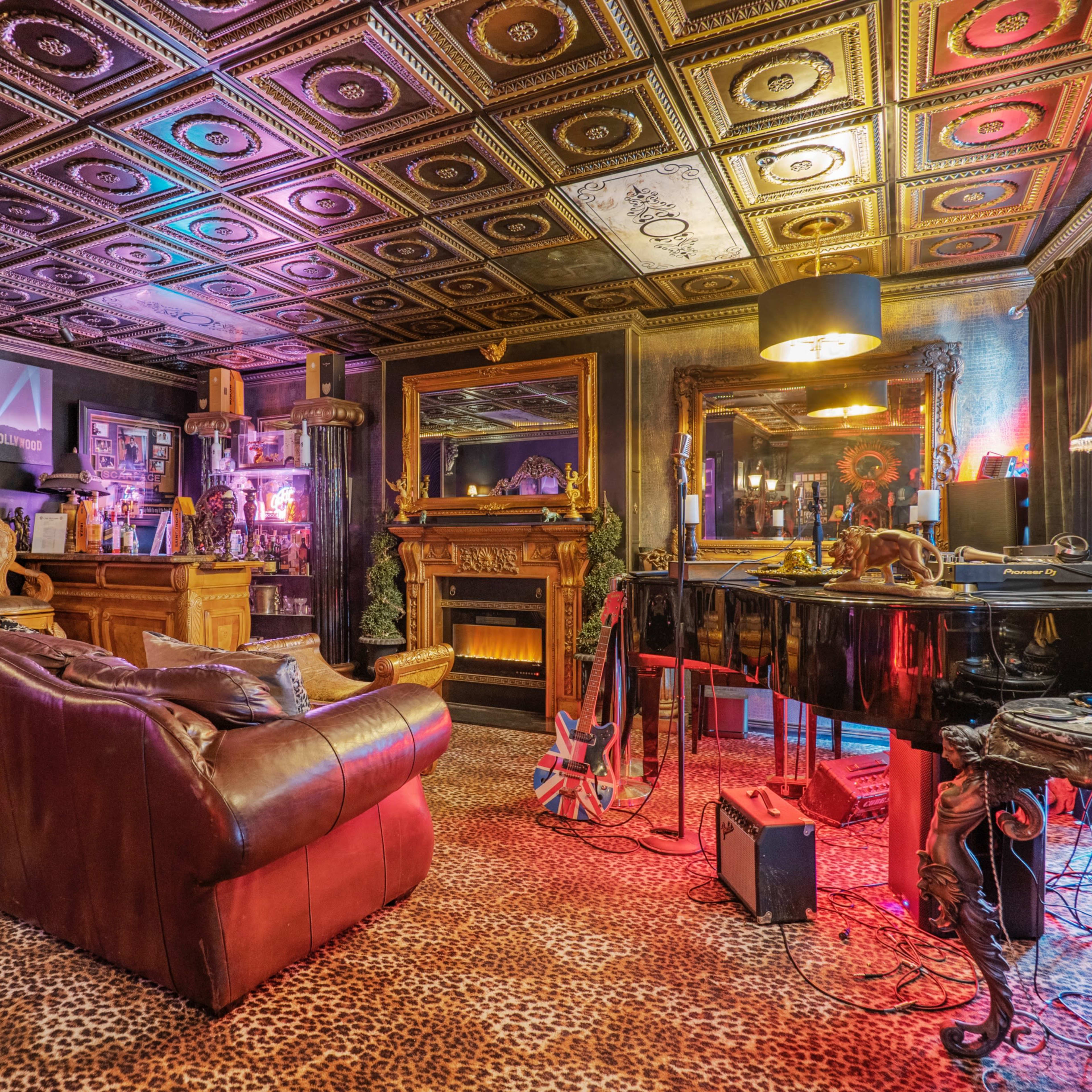 The room features a plush leather sofa, a grand piano, ornate furnishings, and a ceiling adorned with decorative tiles, all set against a backdrop of vibrant lighting and animal print carpet.