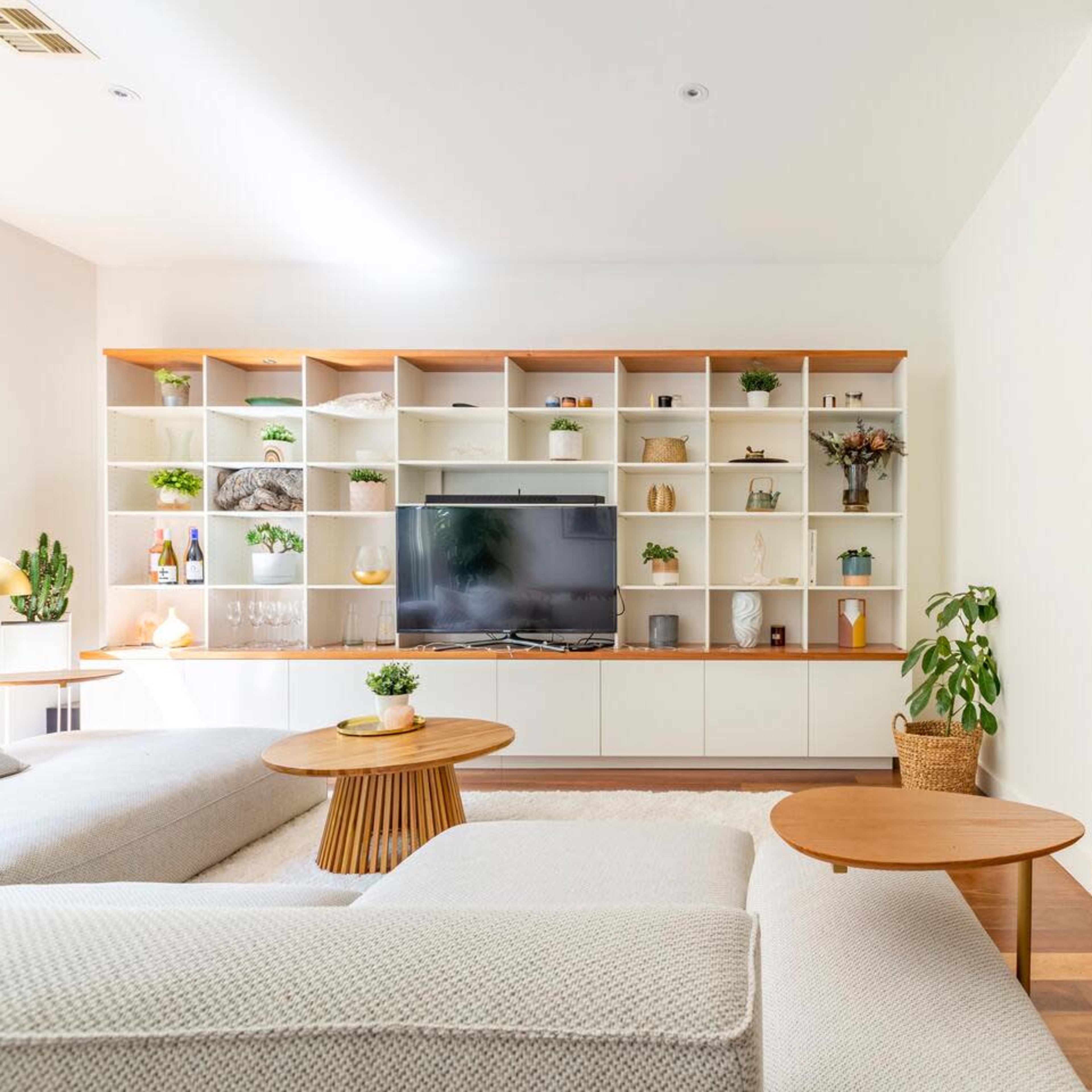 A modern living room with a sectional sofa, a large TV on a white shelving unit, and a small table paired with a plant.