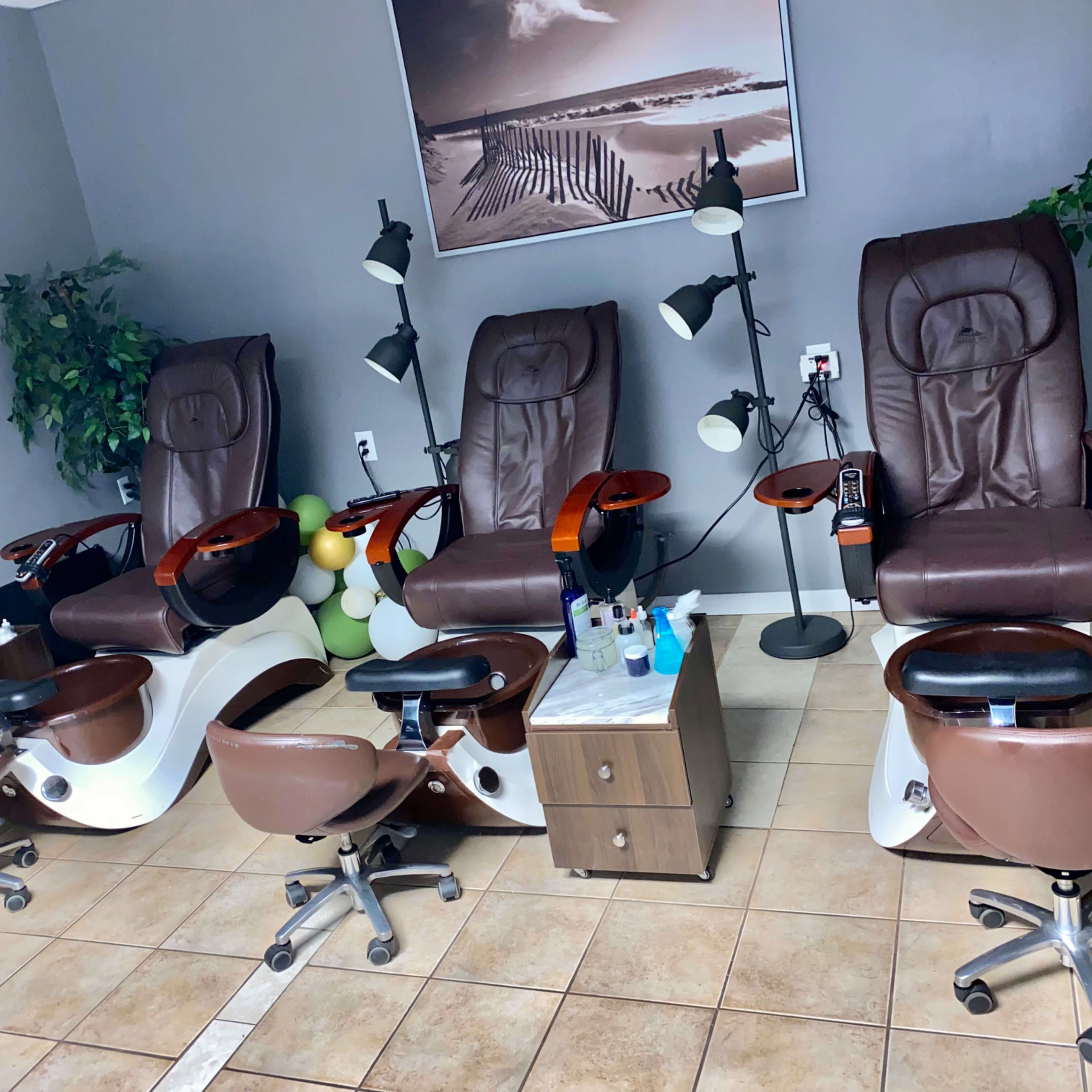 A nail salon interior with five pedicure chairs and several small tables, all arranged neatly against a gray wall.