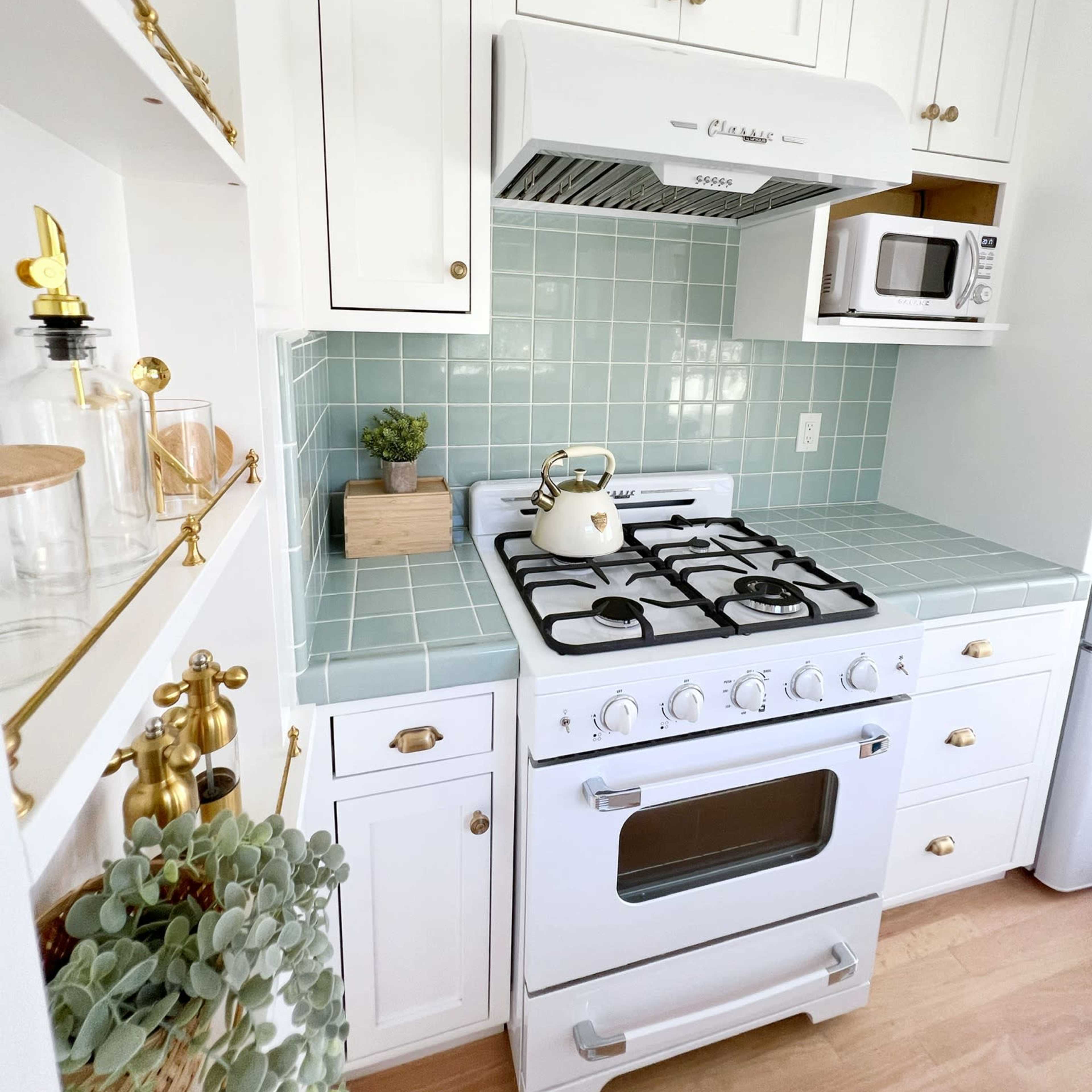 A kitchen featuring white cabinetry, a gas stove with a vent hood, a microwave, and light green tile backsplash.