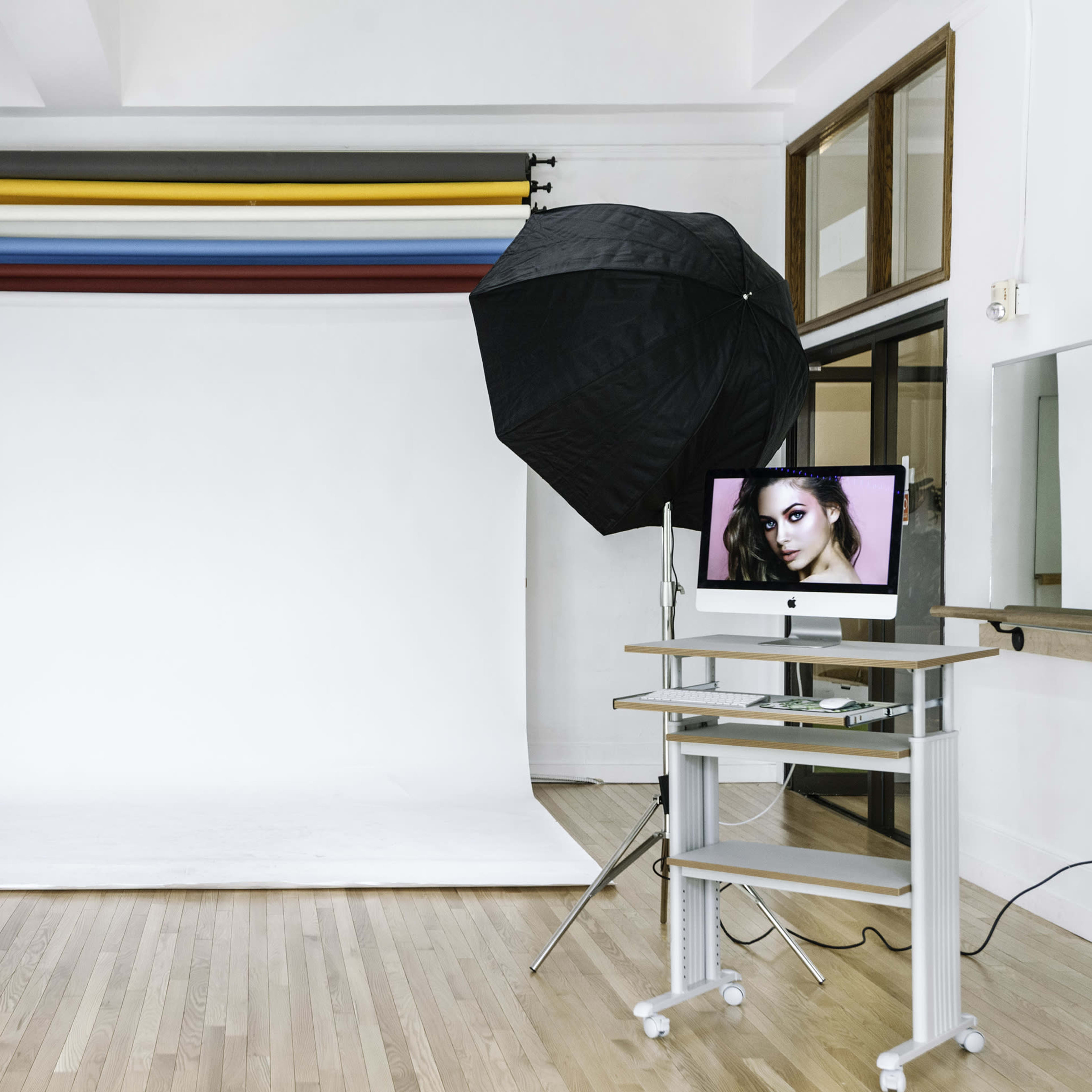 A photography studio with a white backdrop, a lighting umbrella, a ring light, and a computer displaying a model's photograph.