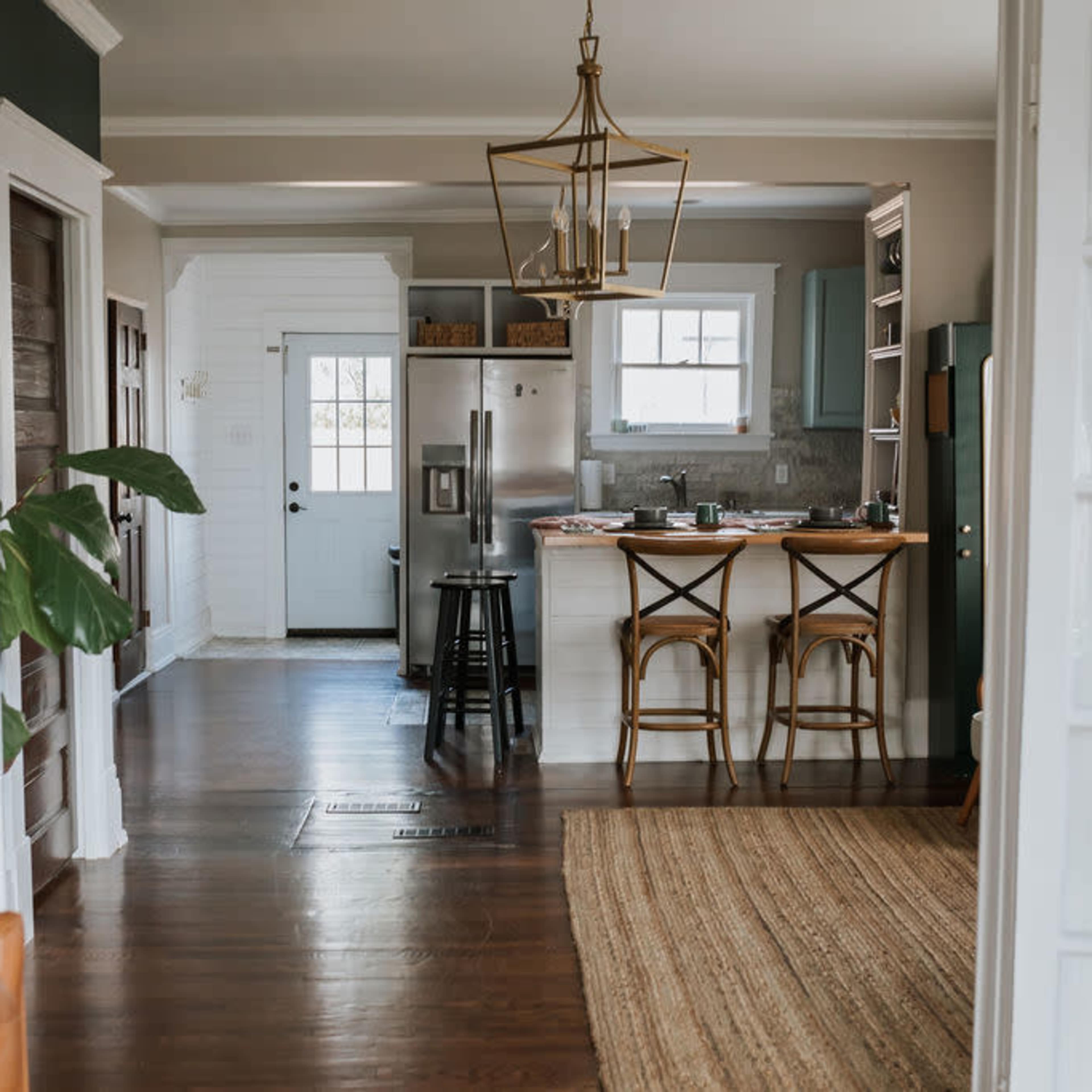 A bright and modern kitchen with an island and bar stools, viewed from a living area through double doors.
