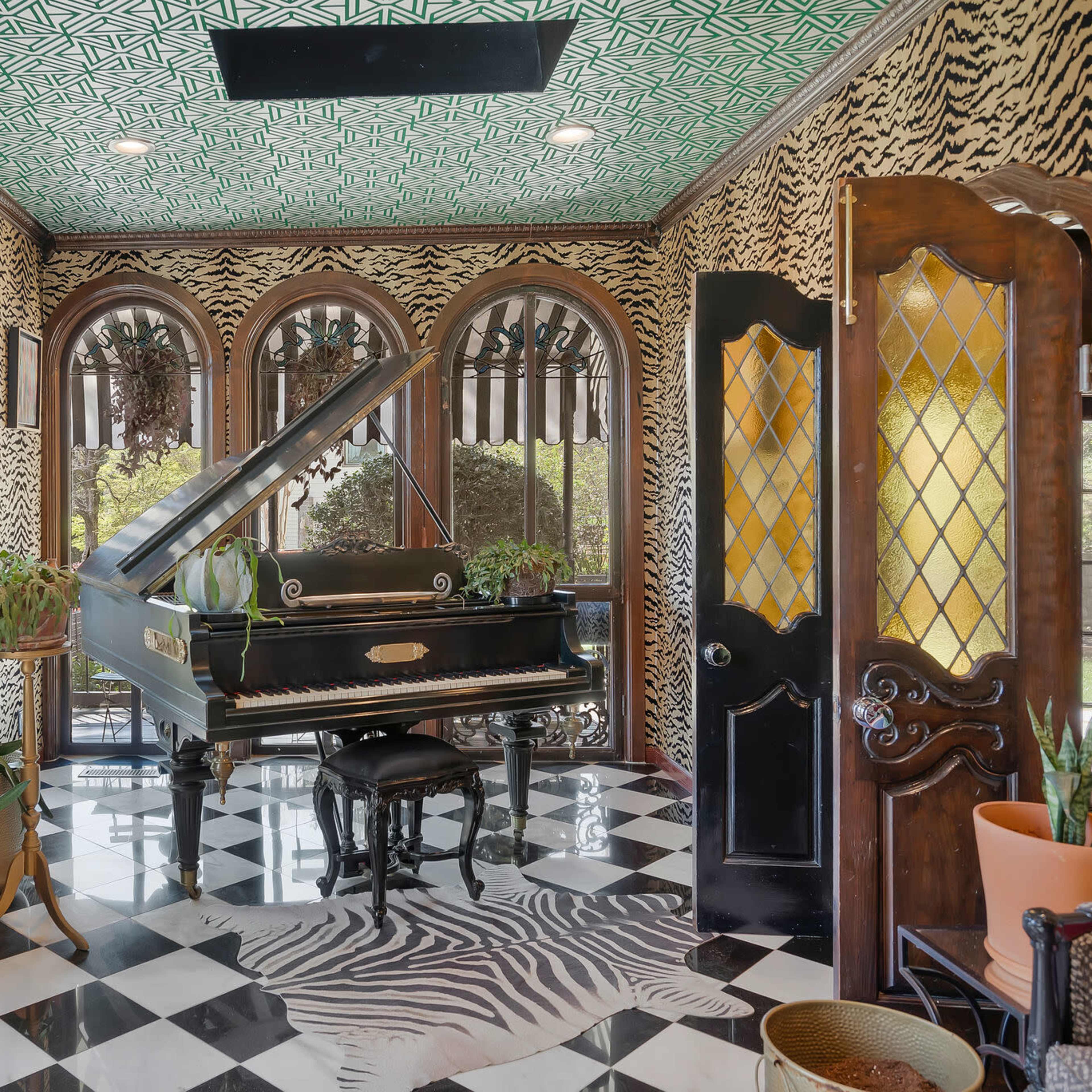 The room features a grand piano surrounded by large windows, patterned walls, and potted plants, with a black and white checkered floor.