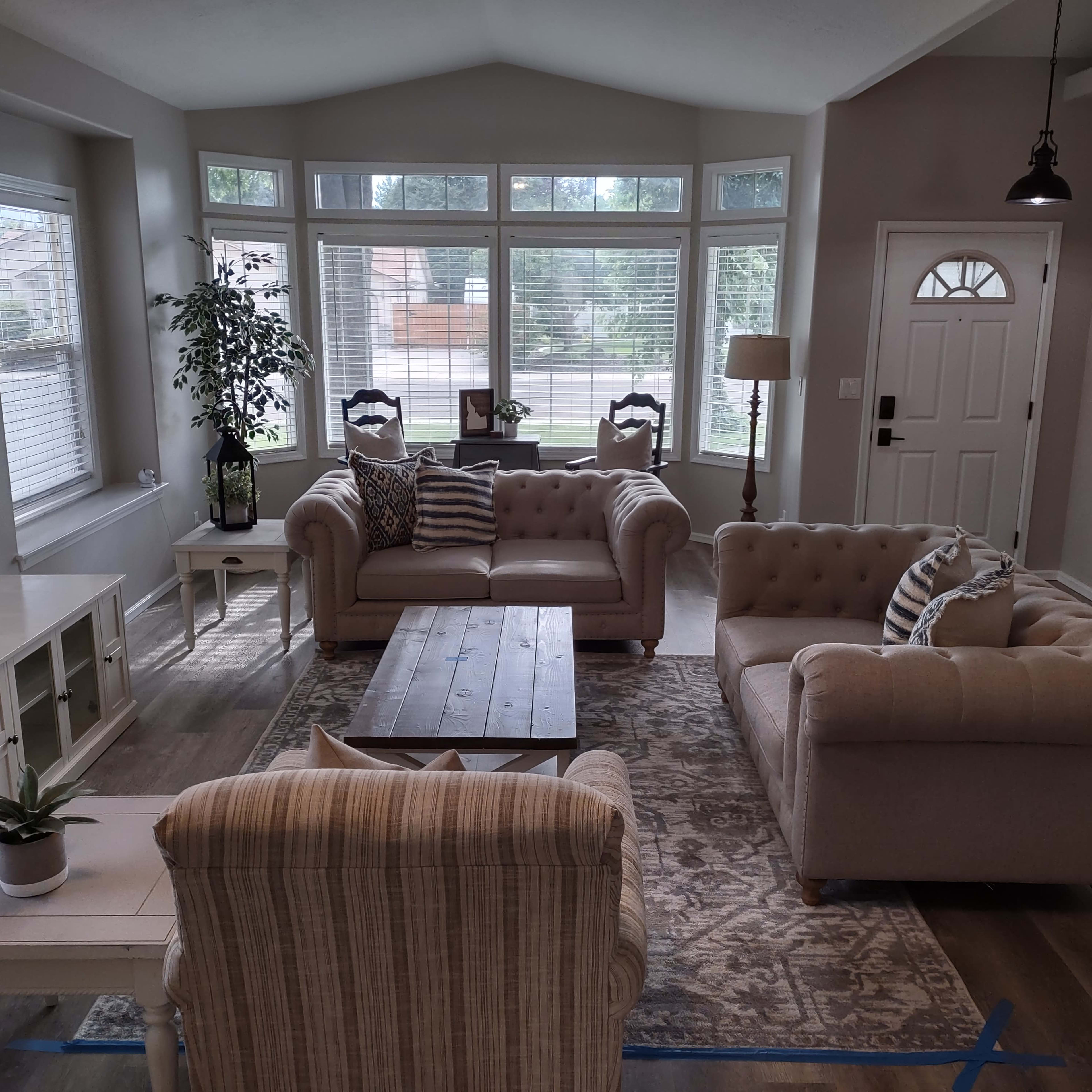 A living room with two beige couches facing a coffee table, surrounded by large windows and a front door.