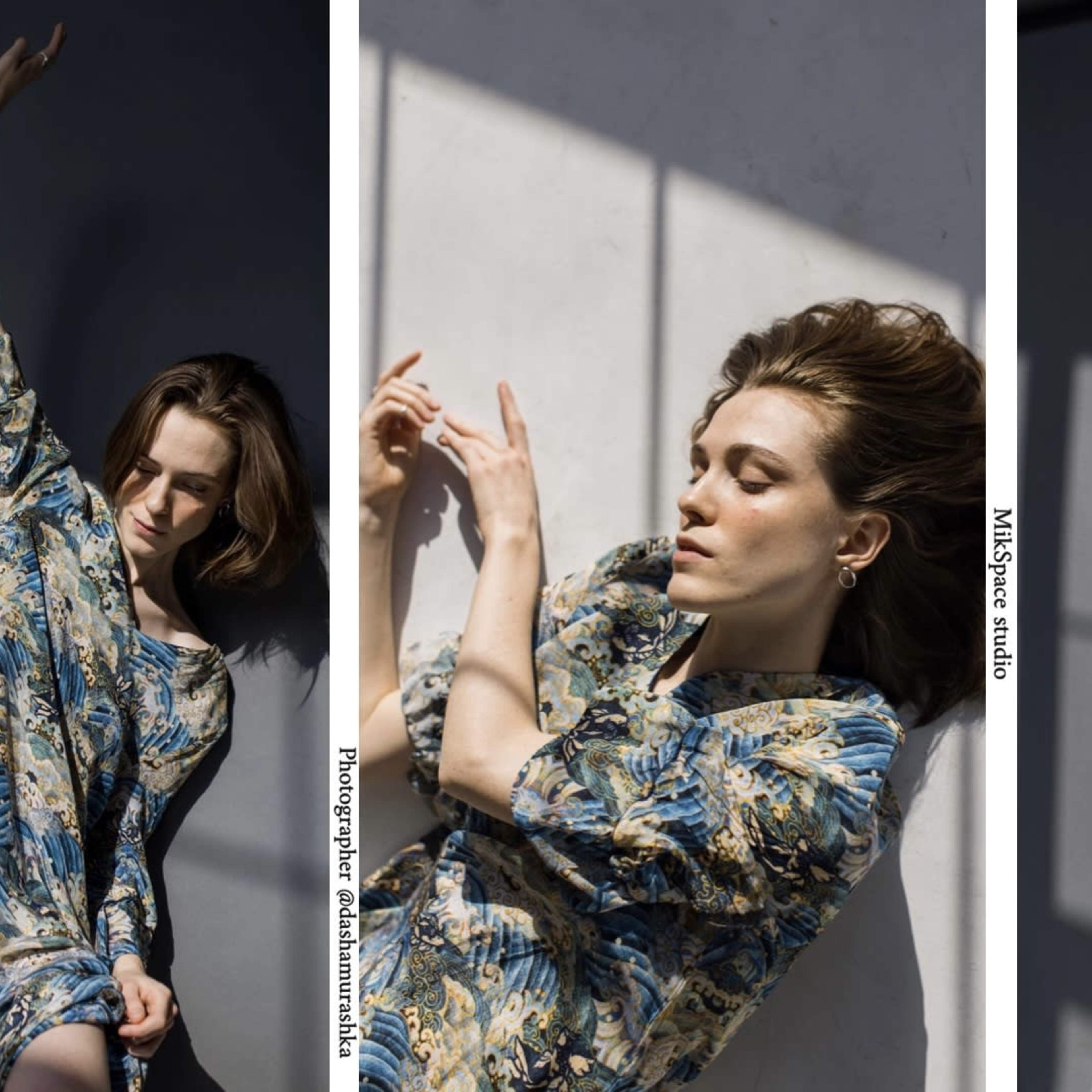 A woman in a floral dress poses in a sunlit studio with dramatic shadows.