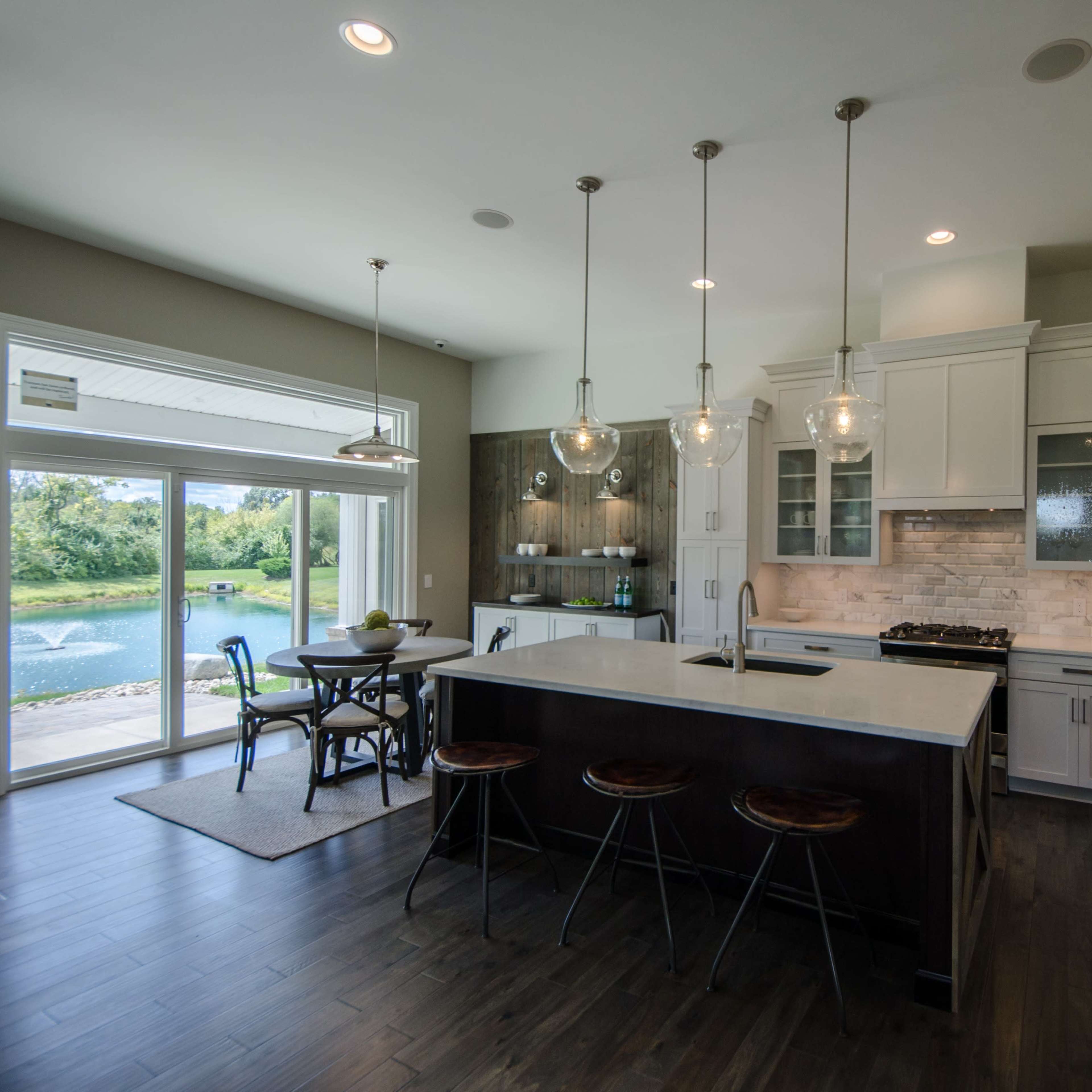 The kitchen features a large island with bar stools, white cabinetry, and a view of a scenic outdoor area through sliding glass doors.