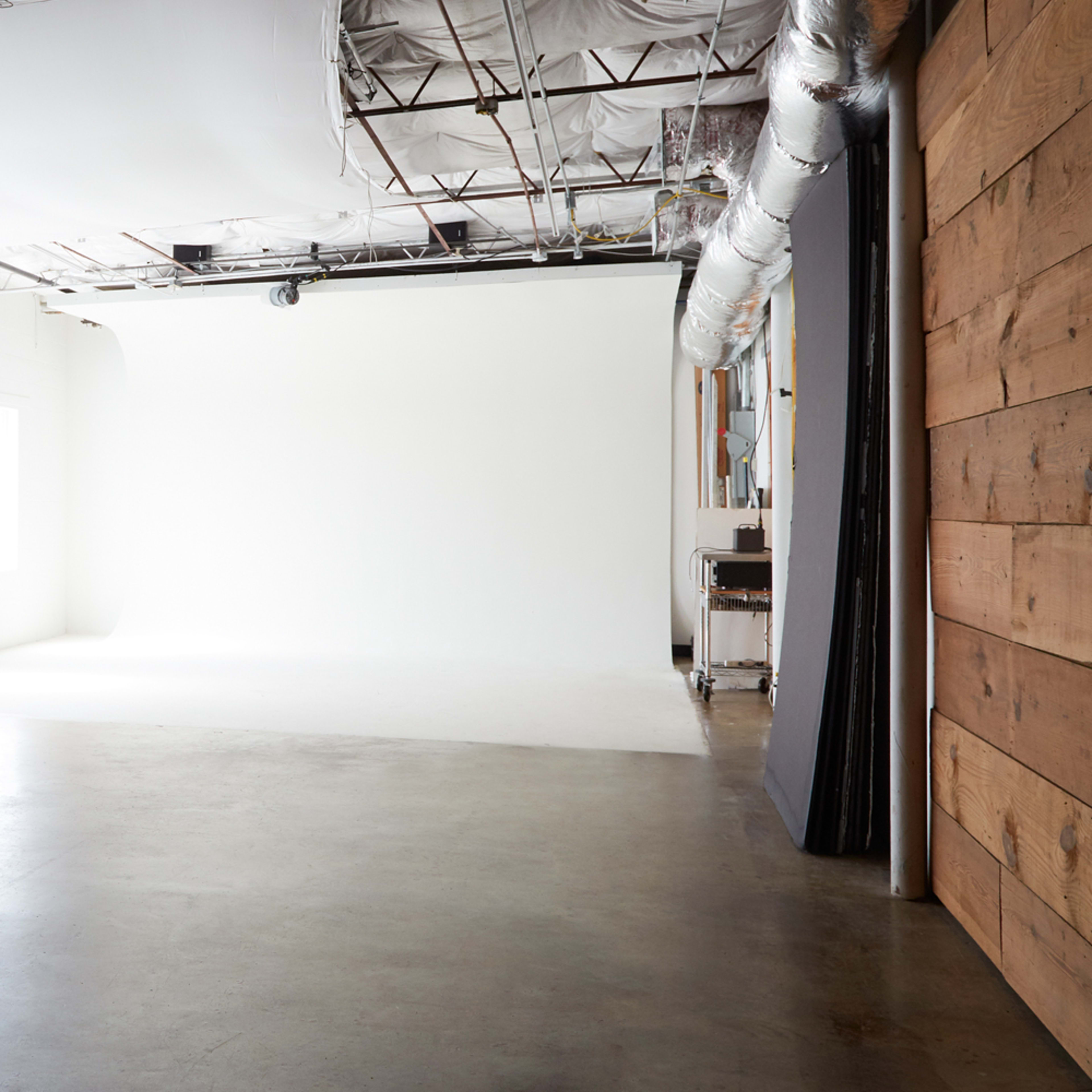 A spacious, empty studio with concrete flooring, white walls, and large windows.