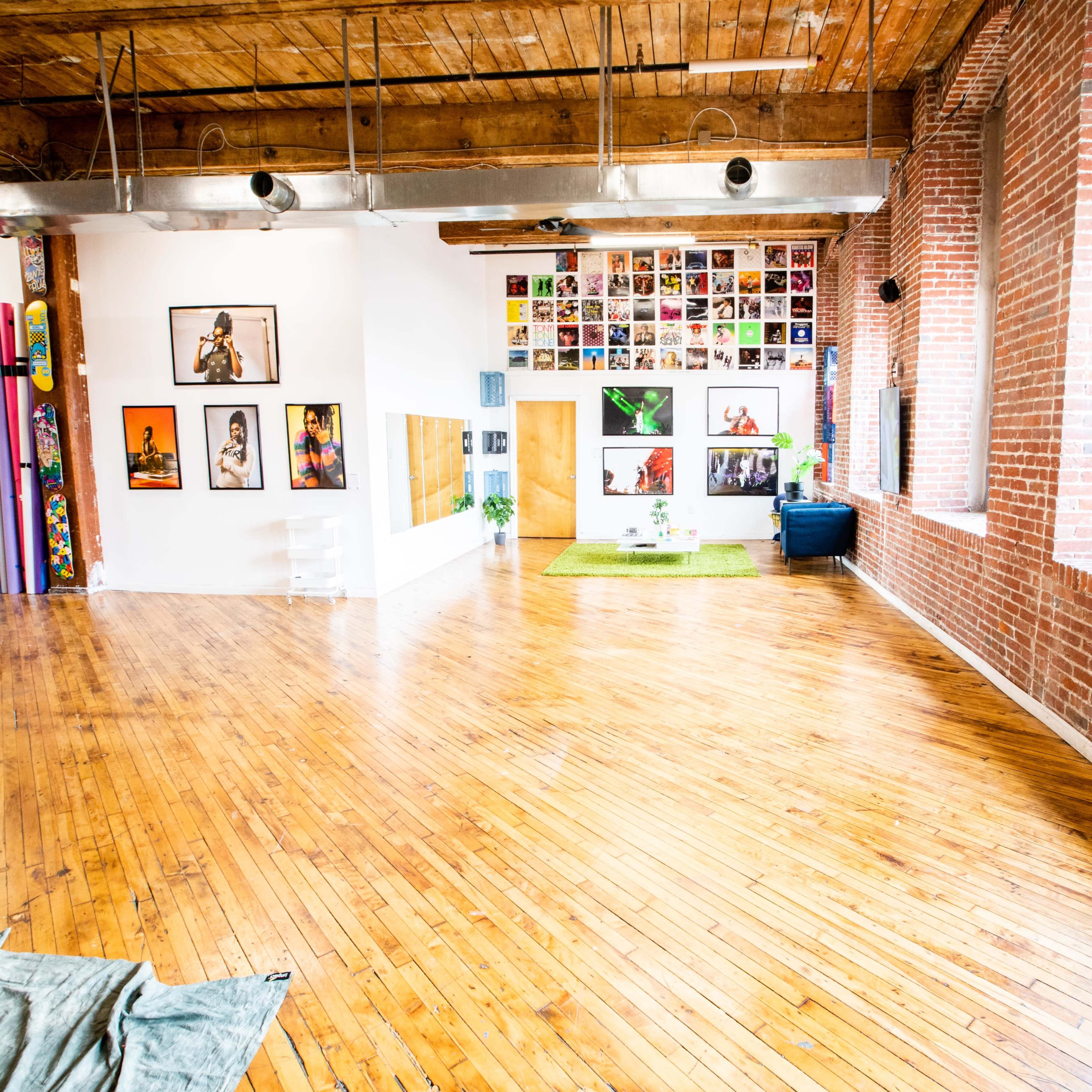 A spacious, brightly lit interior with wooden floors, brick walls decorated with framed photographs, and a small green area with plants.