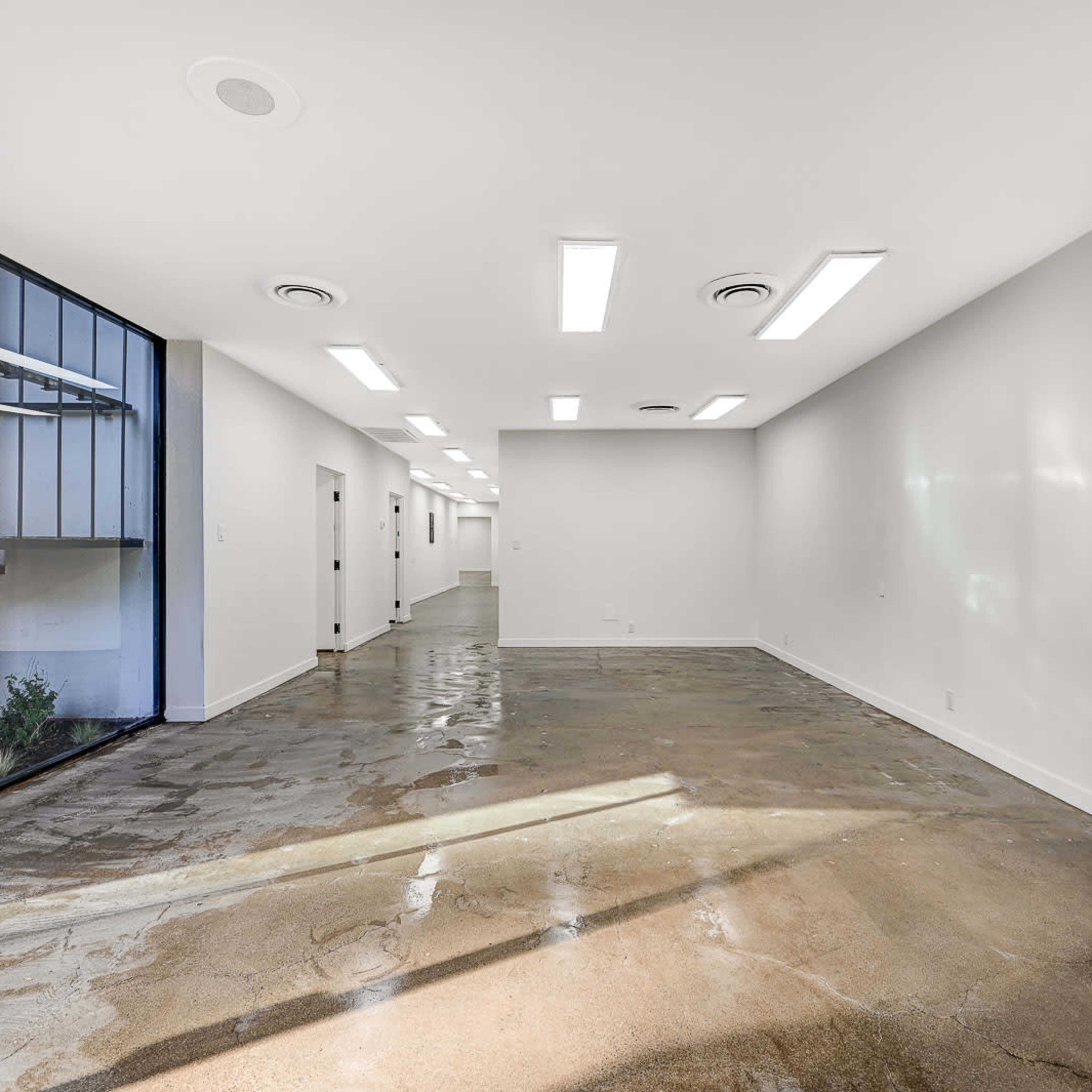 An empty interior space with polished concrete flooring and white walls, illuminated by overhead lighting.