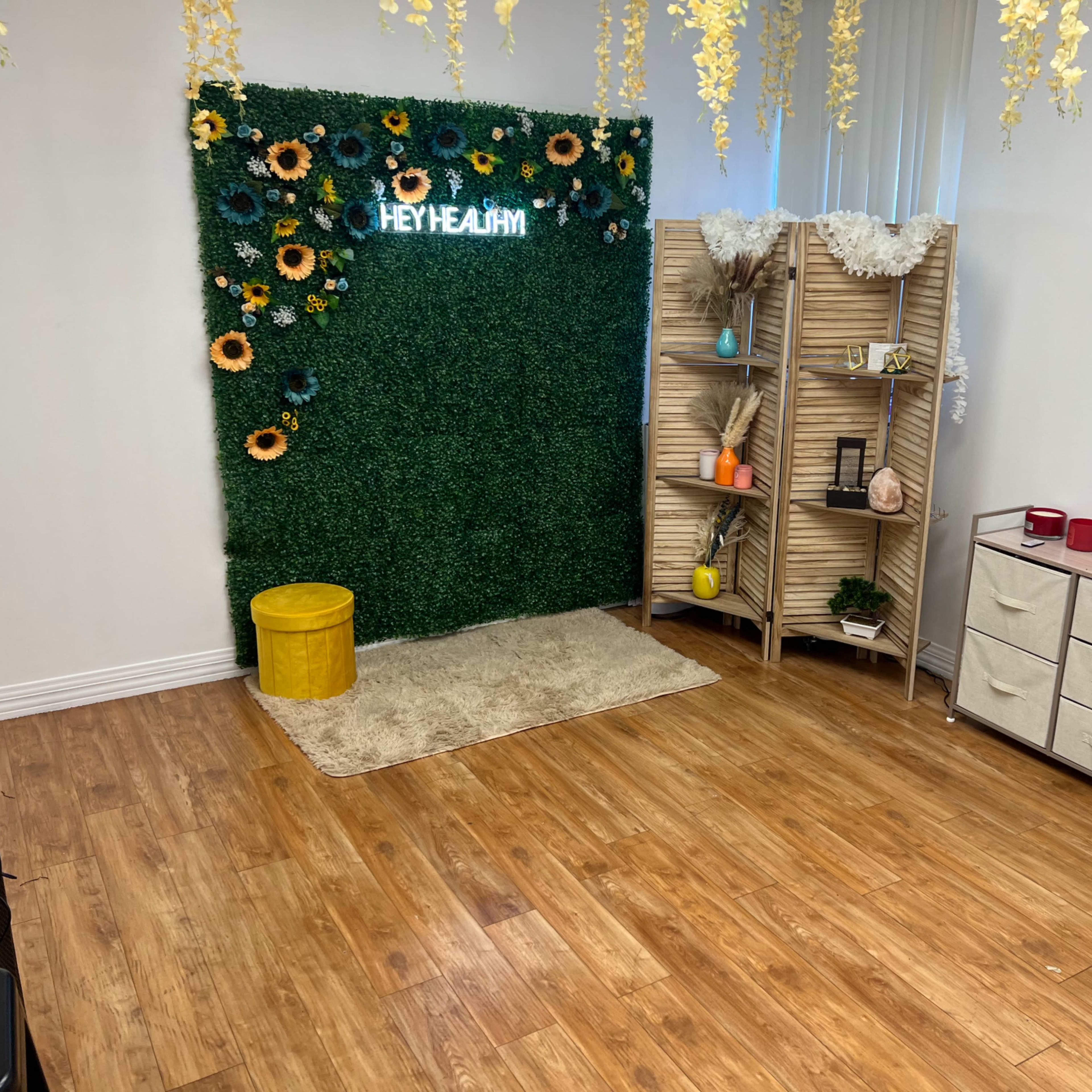 A room with a wooden floor featuring a green wall decorated with sunflowers, a yellow storage container, a rug, a shelving unit with decorative items, and a small dresser.