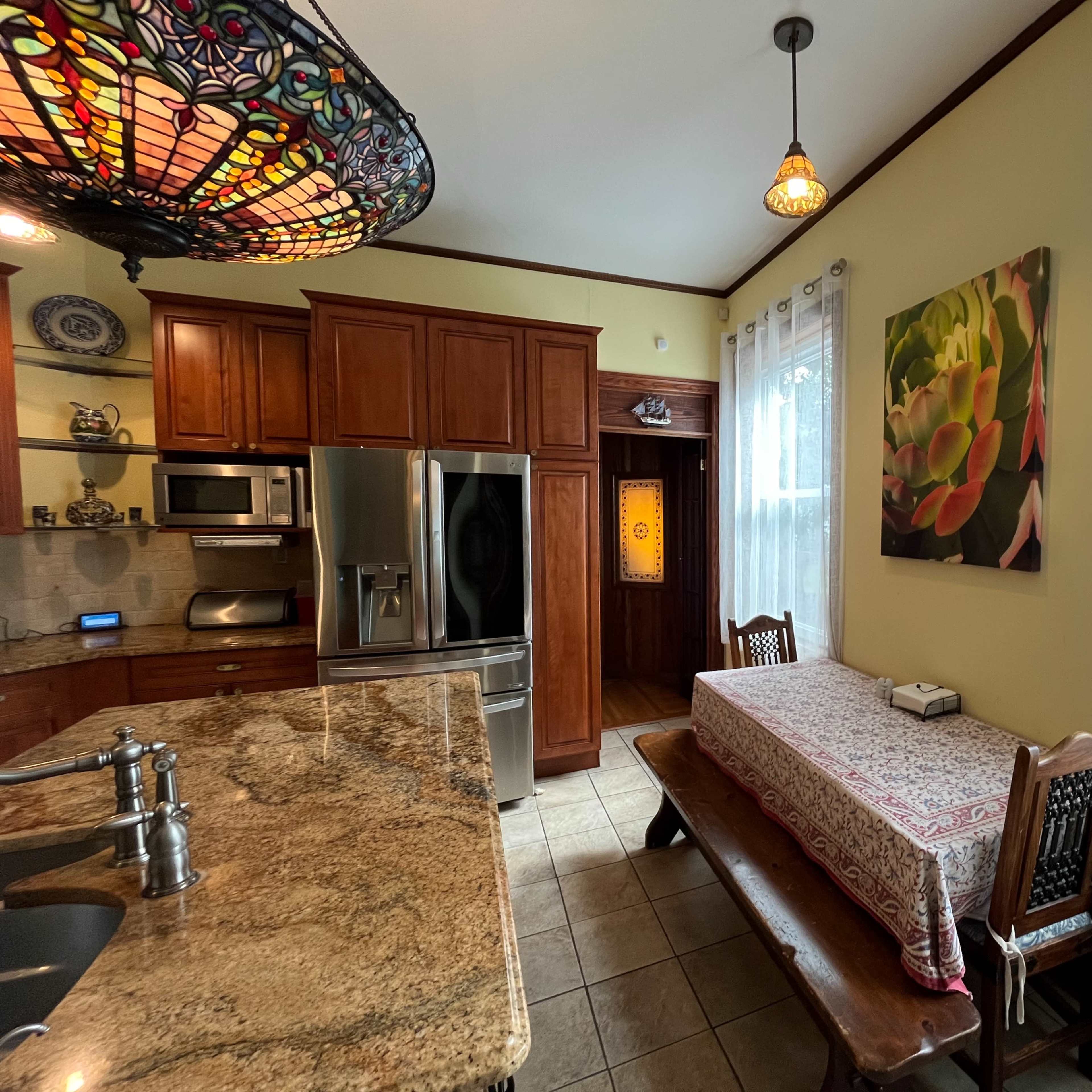 A kitchen featuring wooden cabinetry, a large stainless steel refrigerator, and a dining table with a decorative tablecloth near a window.