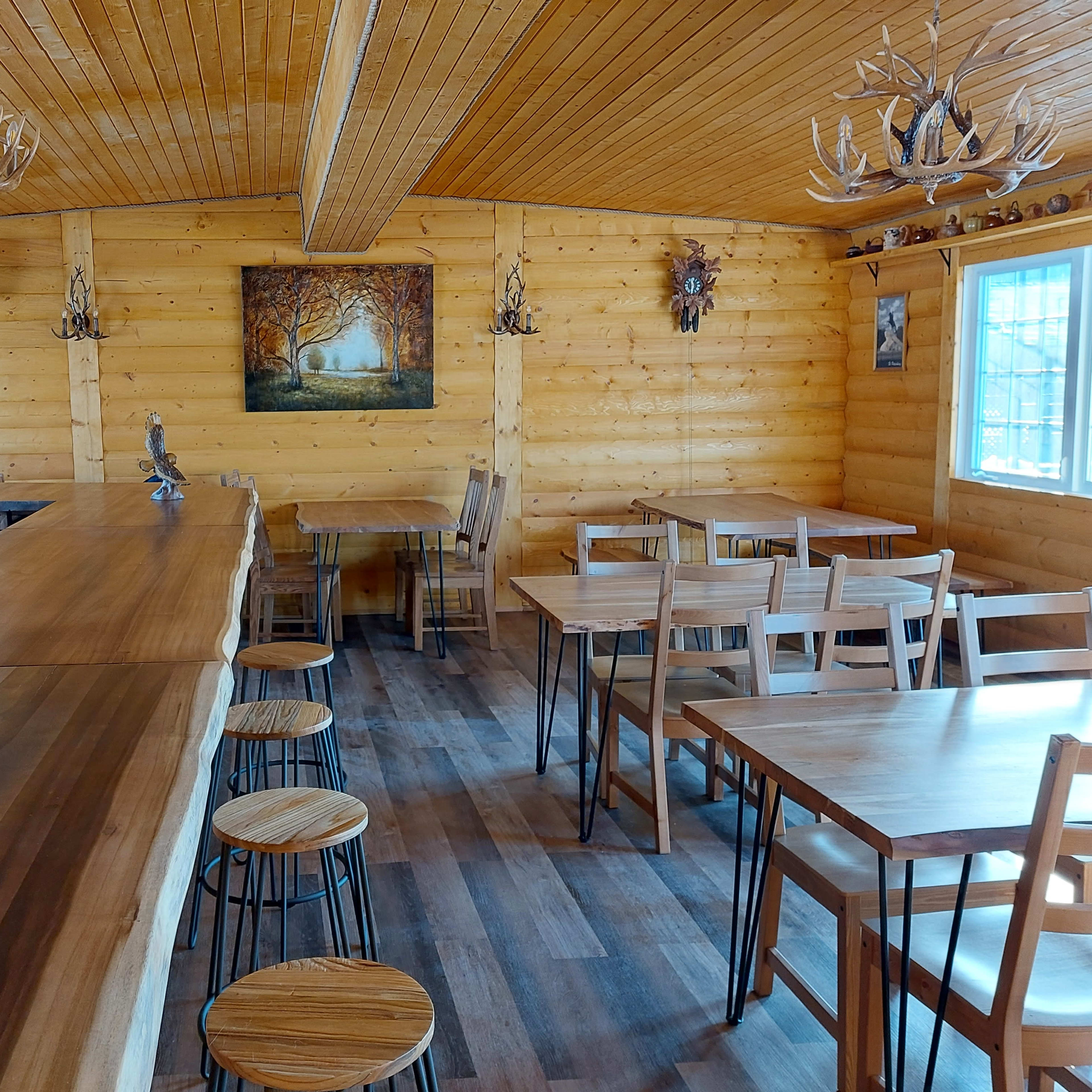 The interior of a log cabin features wooden walls, a long bar made of polished wood, and several wooden tables and chairs arranged throughout the space.