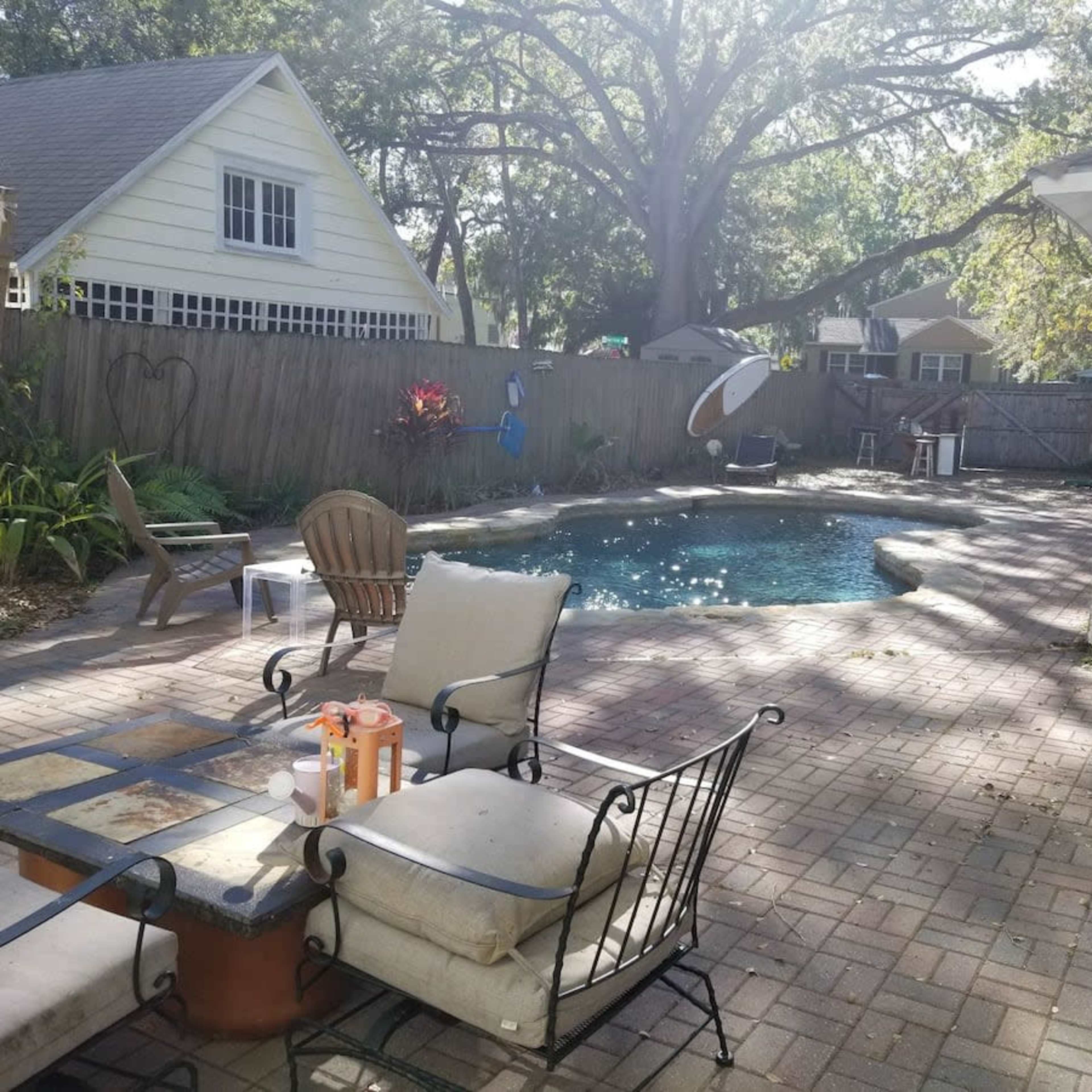 A backyard with a swimming pool surrounded by a patio, lounge chairs, and greenery.