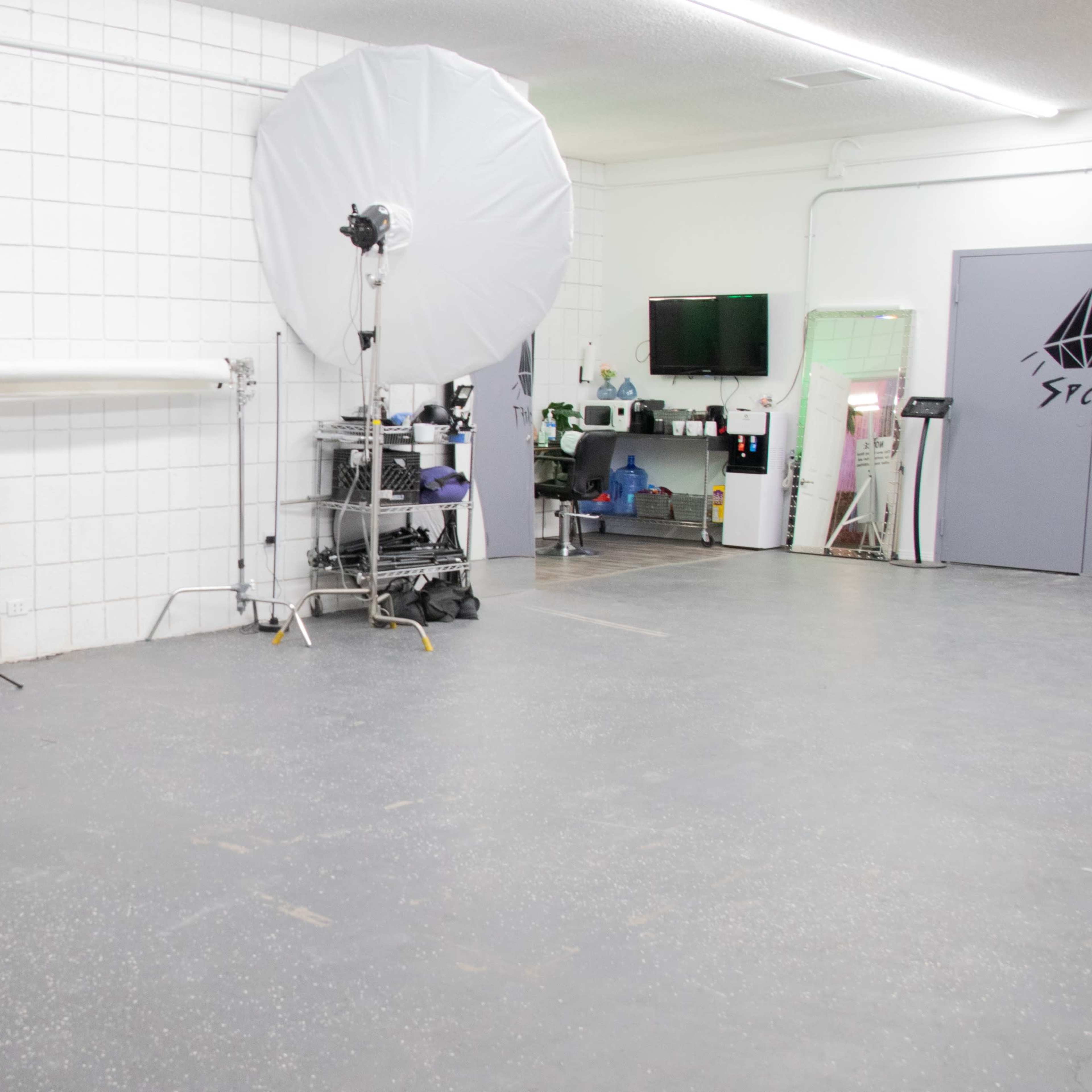 A spacious studio with a round table and chairs, two large softbox lights, and various equipment along the wall.