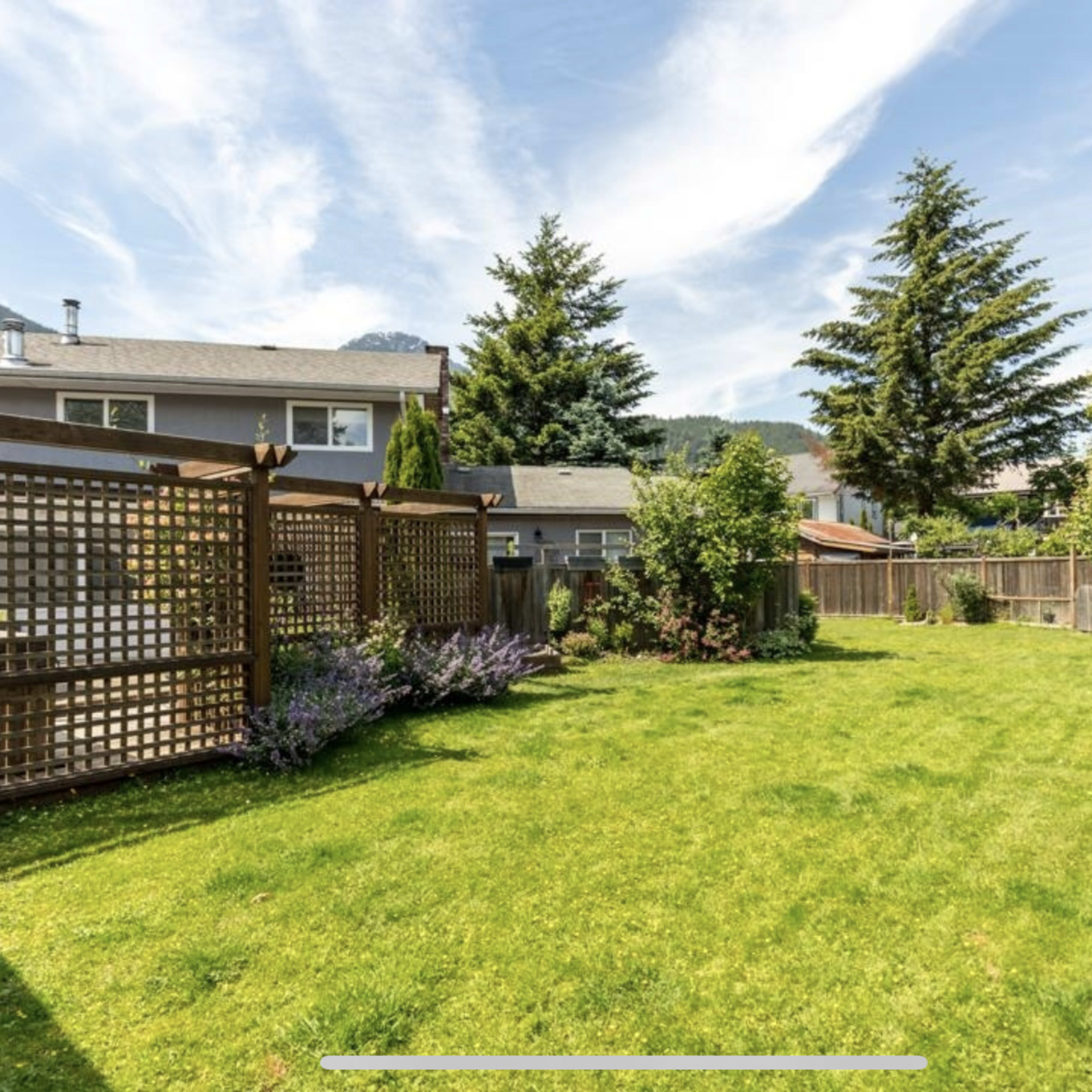 A spacious lawn surrounded by wooden fencing and greenery, with houses in the background under a clear blue sky.