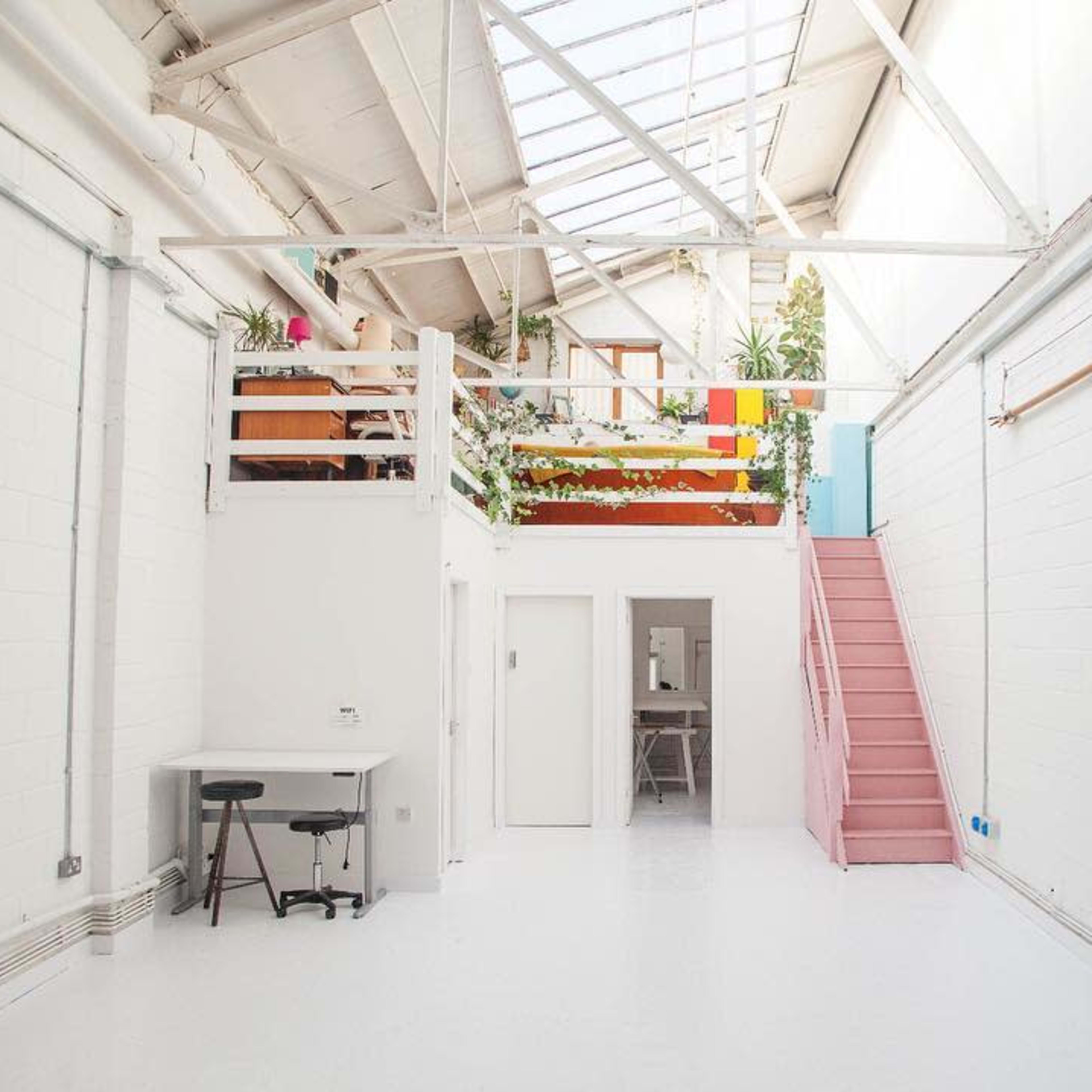 A bright, minimalist interior space with white walls, a staircase, and a loft area adorned with plants.