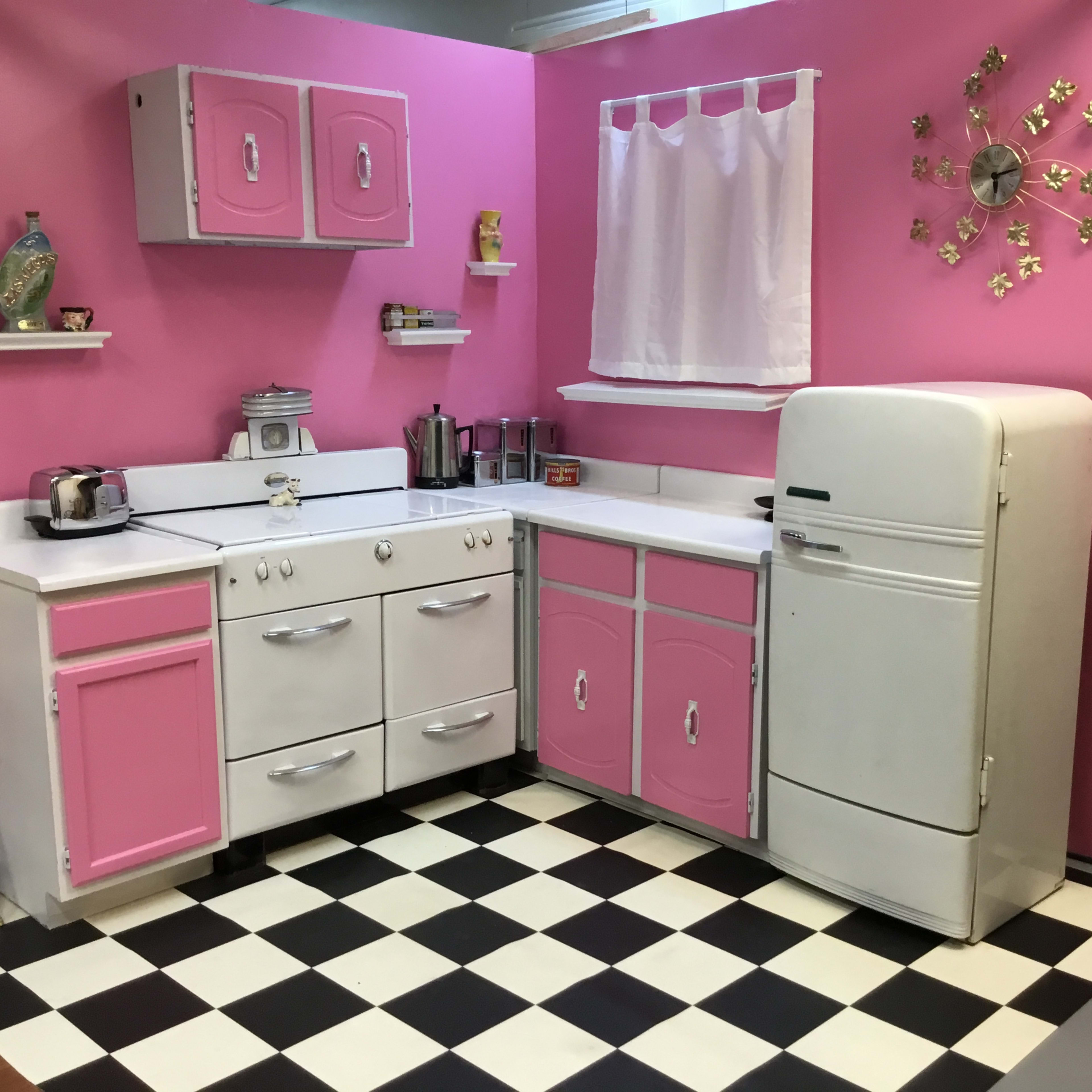 A vintage-style kitchen with pink walls, a checkered black and white floor, and white appliances, including a fridge and stove.
