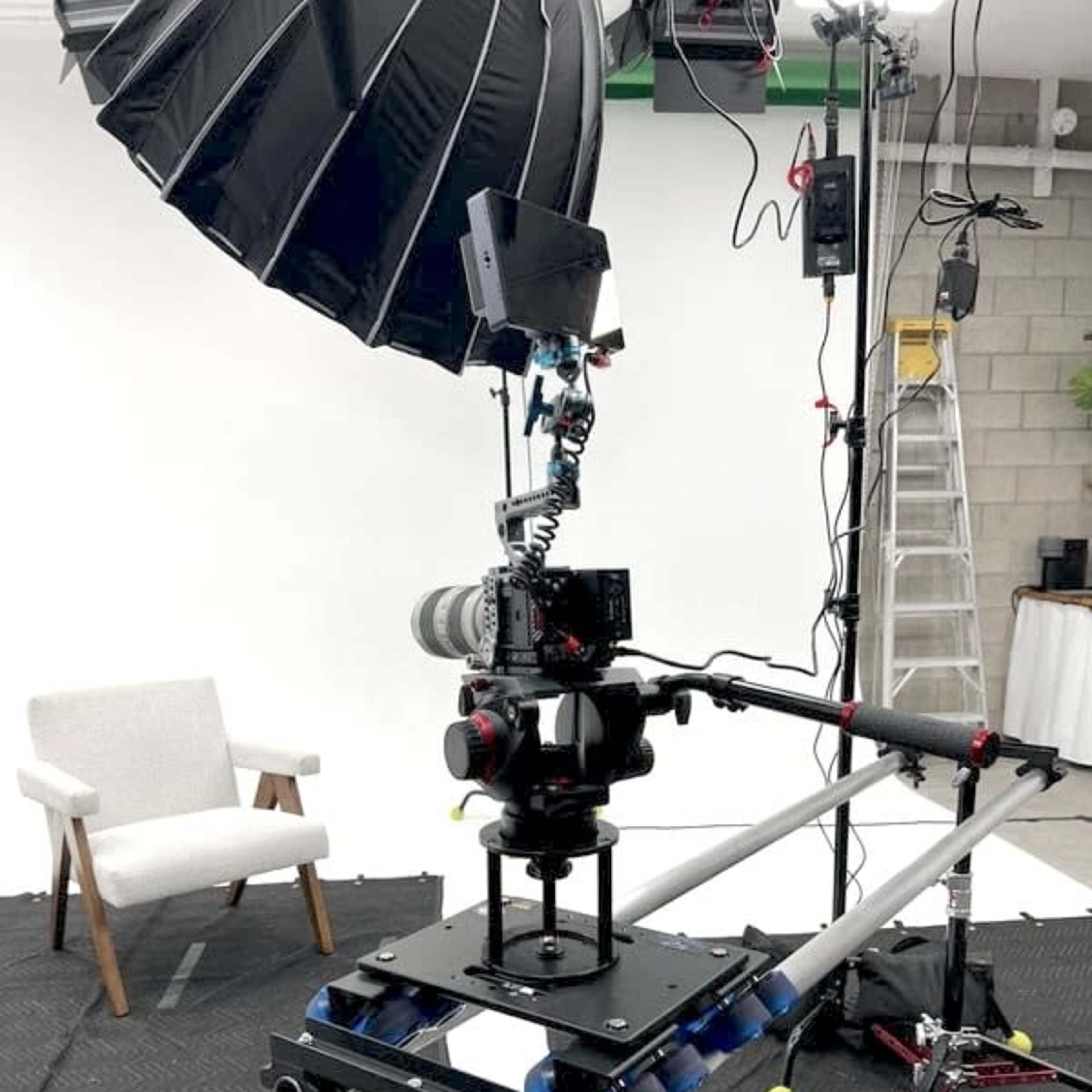 A camera setup on a moving slider with a large umbrella softbox and a chair in a studio environment.