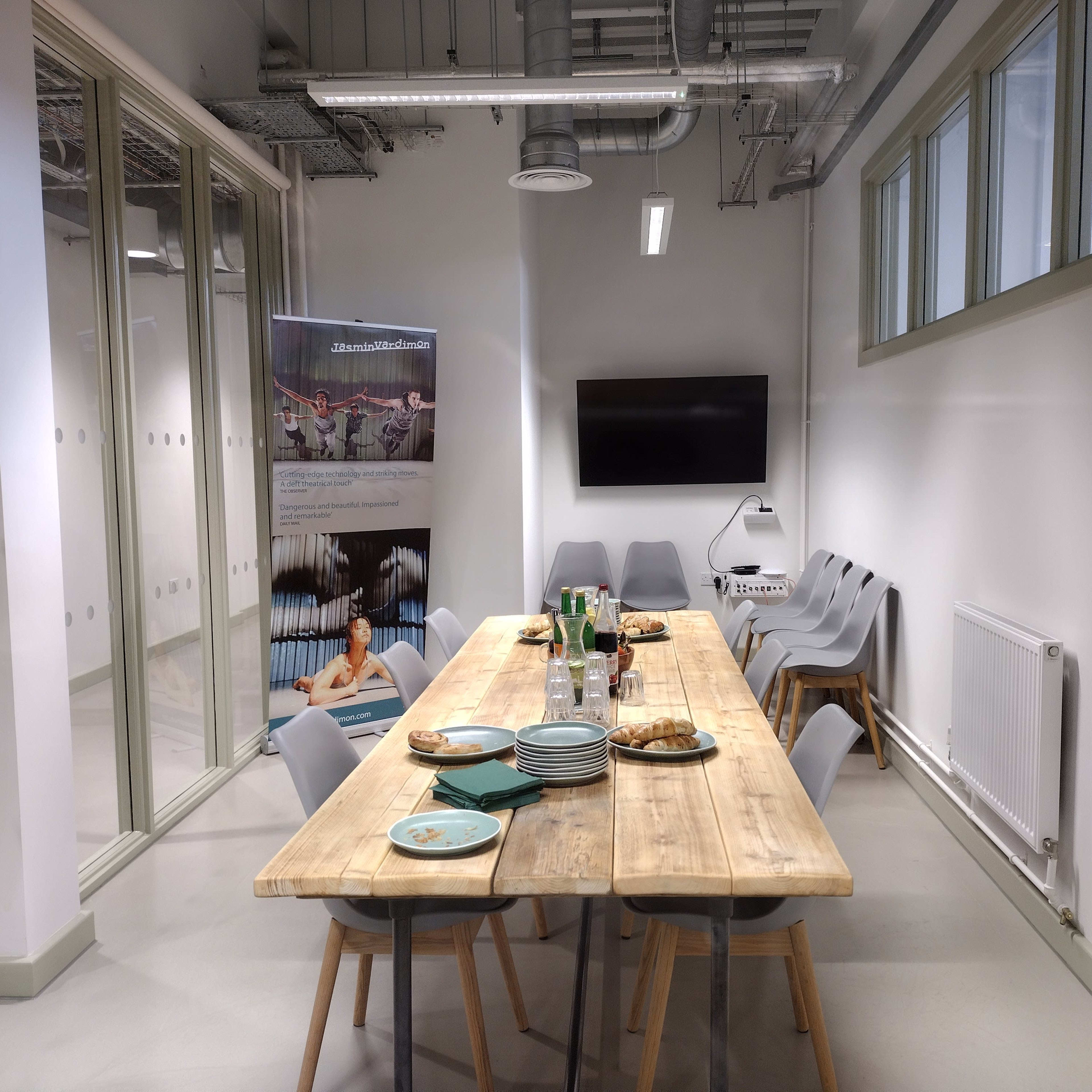 A wooden table is set with plates and food, surrounded by gray chairs in a well-lit meeting room.